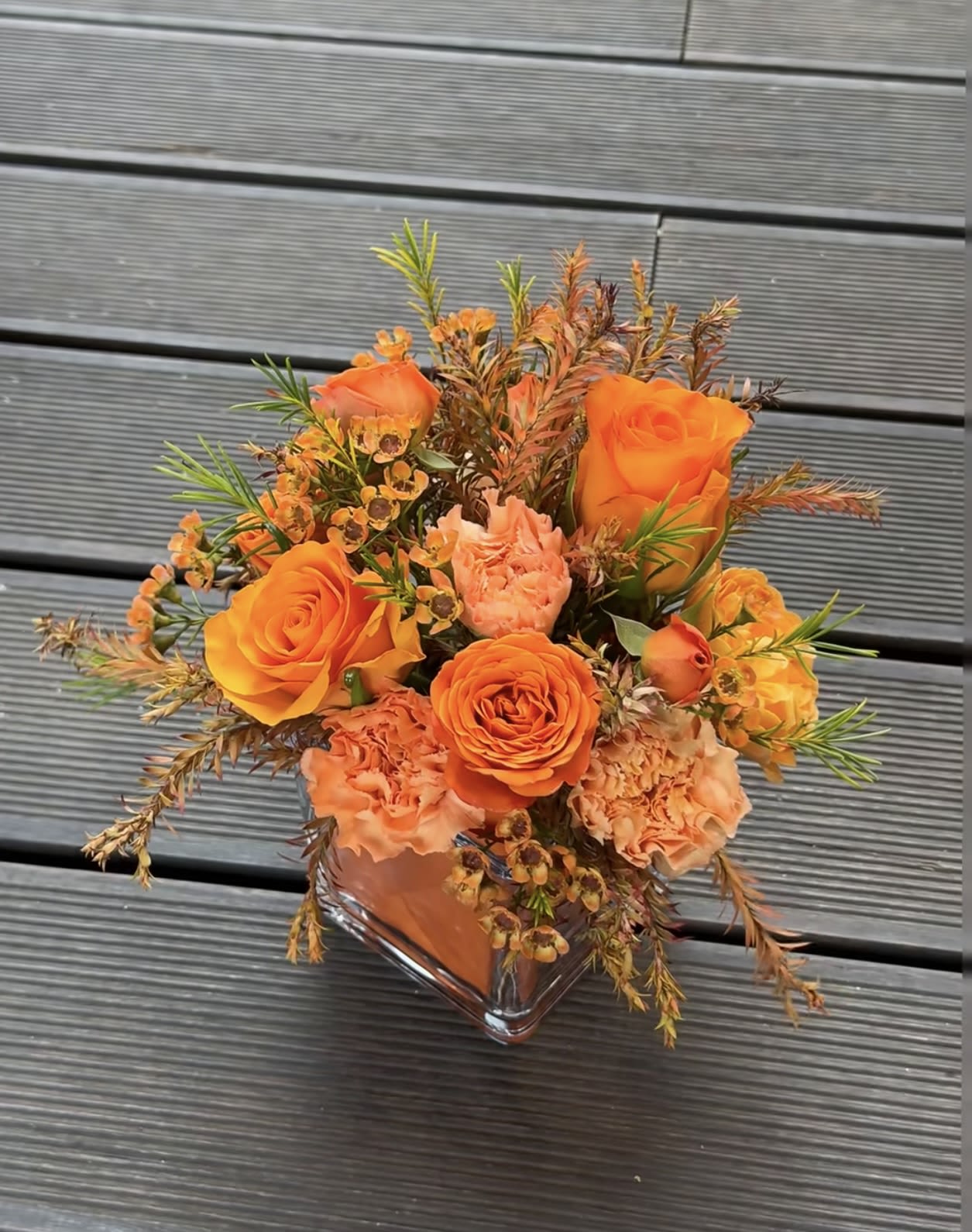 Harvest Glow Centerpiece（Table flowers） - The image shows the price for one square table centerpiece. If you need more, please place your order in multiples. The product includes orange roses, orange carnations, spray roses, waxflower, and a square glass vase. Plant in flower mud. glass vase 4 x 4 x 4 inch