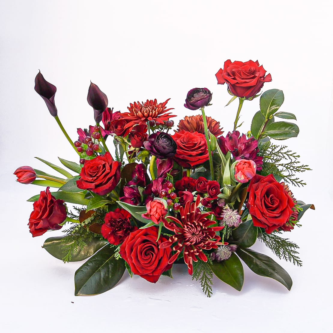 Miracle on 34th Street Centerpiece - The miracle of the holidays is here! Full red and burgundy blooms are the star, framed by deep and luxurious winter greens. Classic and timeless, this arrangement style will elevate any holiday gathering.  Approximate size is 24&quot;W x 12&quot;H