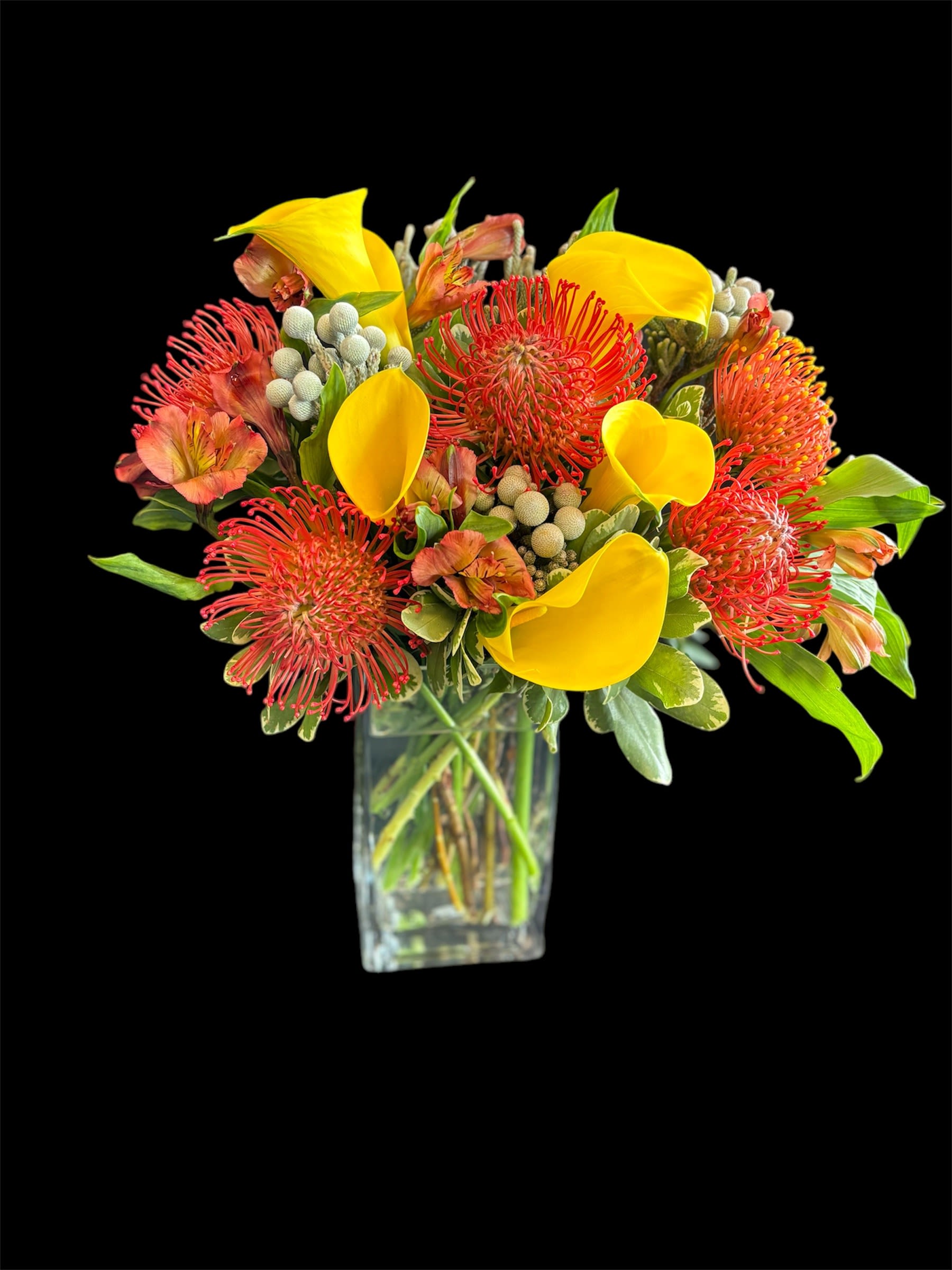 Sunburst Symphony - Vibrant orange protea, bright orange alstroemeria, and sunny yellow calla lilies in a rectangular glass vase.
