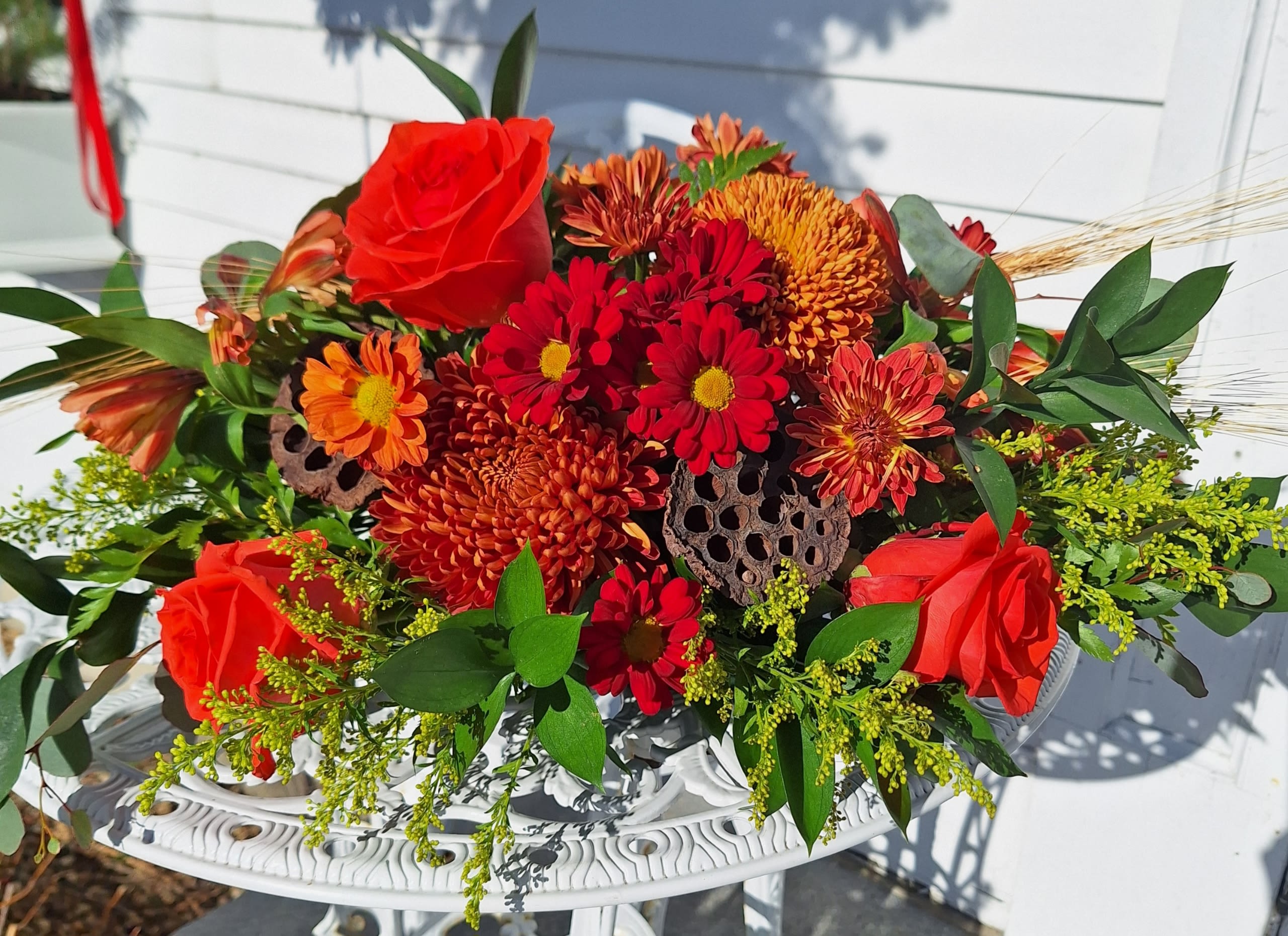 Table Centerpiece - Long and low centerpiece with orange roses, alstroemeria, bronze mums, red daisies, solidago pods and wheat