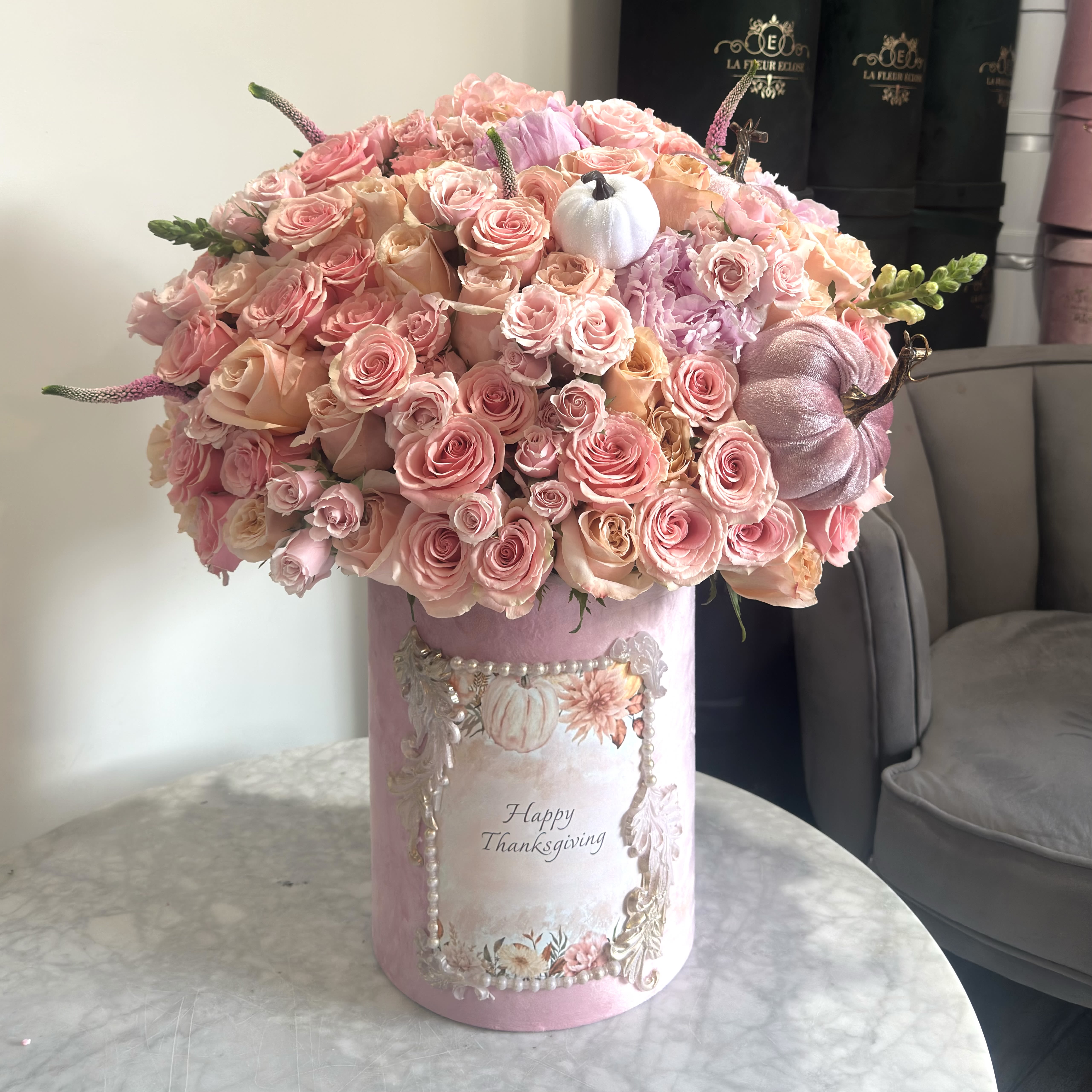 Blush Thanksgiving Bloom Box - Pink Harvest Luxe Arrangement is an exclusive designer floral composition by La Fleur Éclose, created in a soft blush-pink palette with elegant seasonal details.  This luxurious arrangement features a rich blend of premium roses in multiple blush tones, delicate garden textures, soft hydrangea accents, and hand-painted decorative pumpkins for a unique Thanksgiving touch. Each piece is beautifully presented in our signature velvet hat box, embellished with custom artwork created especially for our Thanksgiving Collection.  Perfect for: • Thanksgiving celebrations • Elegant hostess gifts • Home and holiday décor • Expressing gratitude • Making a memorable impression  Every arrangement is handcrafted with love and may vary slightly, making each piece truly one-of-a-kind.
