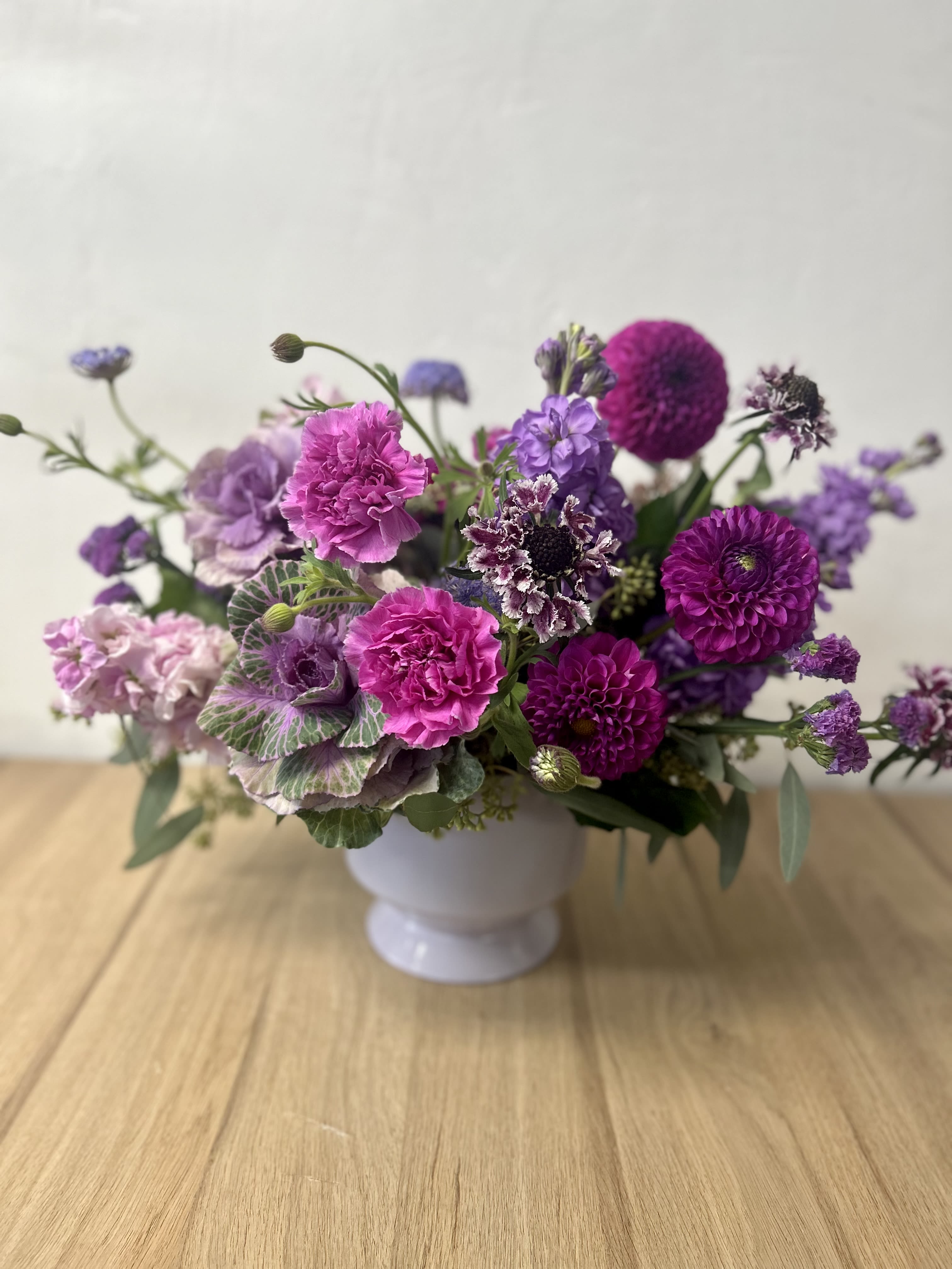 Lavender Haze - A fun combination of purples and lavenders, in a ceramic compote vase. Made up of ornamental kale, stock, scabiosa and other seasonal florals.  **All arrangements will vary slightly based off seasonal availability. **