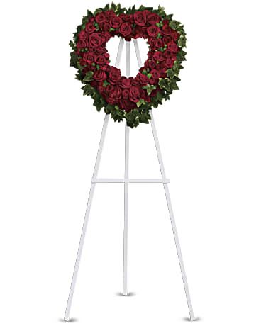 Blessed Heart Spray - Make a bold and elegant statement of love with our stunning heart-shaped wreath at FloristMarketplace. Set on a funeral easel, this rich red rose sympathy arrangement serves as a beautiful standing spray, perfect for placing on the altar or at the entrance of the service.  Featuring a lovely combination of red roses and carnations, accented with ming fern and variegated ivy, this open heart-shaped wreath is designed to honor cherished memories. It comes presented on a traditional wire easel for easy placement.  Orientation: One-Sided.   