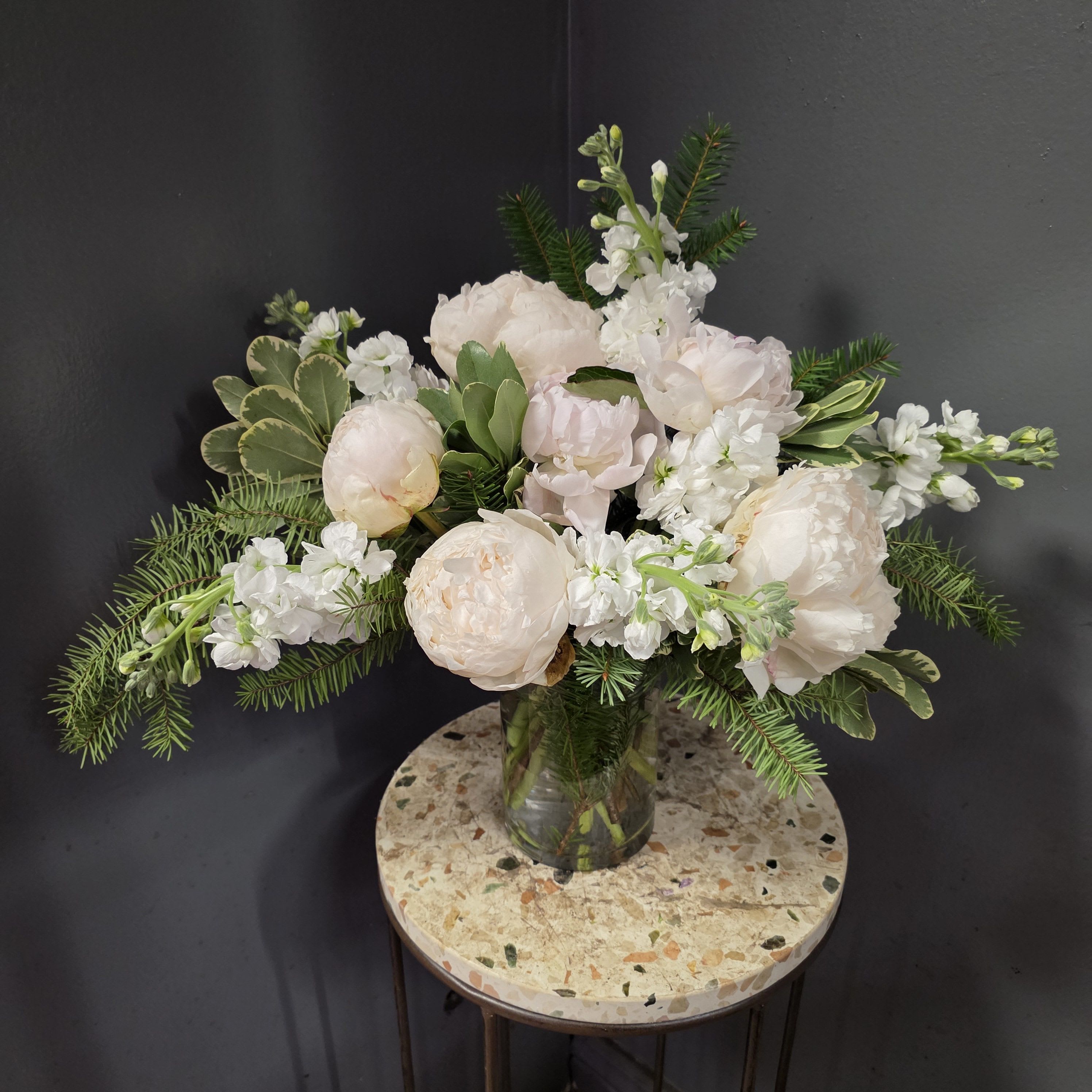 Poetic Peonies - Soft, romantic, and perfectly winter-chic, our Poetic Peonies arrangement features premium blush-ivory peonies paired with fragrant white stock, lush winter greens, and variegated foliage. This airy, garden-style bouquet captures the timeless elegance of fresh peonies while adding a subtle seasonal touch with evergreen accents.  ***This bouquet is seasonal, and white peonies sometimes have to be ordered a few days ahead of time***  Designed by our team of luxury florists in Centennial, this arrangement is ideal for winter celebrations, holiday gifting, home décor, sympathy flowers, or anyone who loves soft white florals with modern texture. Its ruffled peonies and snow-white palette bring a sense of calm beauty to any room.  Available for same-day peony delivery in Denver, Centennial, Highlands Ranch, Lone Tree, Greenwood Village, and Cherry Creek. Also available for in-store pickup at Zalea Flowers.