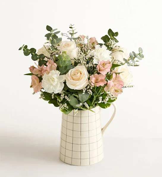 Natural Elegance™ Bouquet - About Natural Elegance™ Bouquet NEW In Britain, “pale and interesting” is a compliment given to someone with a delicate, enticing elegance. It also applies to this luscious gathering of roses, Peruvian lilies, and other blooms in white and peach tones, accented with shapely greenery. The bouquet is arranged by hand in our pitcher-shape ceramic vase, which only adds to its charm.