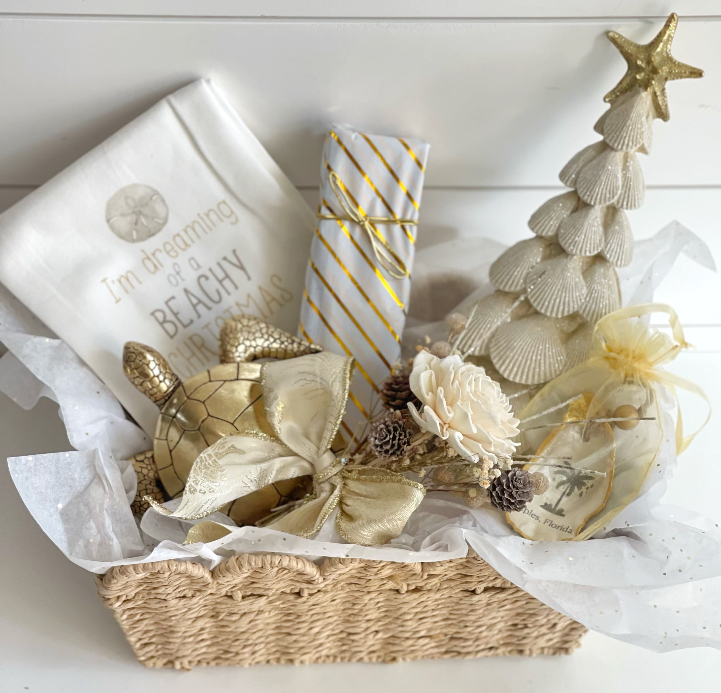 I’m Dreaming of a Beachy Christmas-Gold - This Christmas gift basket is elegant and Beachy! It includes: -“I’m dreaming of a Beachy Christmas” 100% cotton dish towel. -gold decorative Sea Turtle -gold and pearl shell decorative Christmas tree -Christmas shell ornament made locally by Naples artist in an organza bag -Norman Love Confections 5 piece Black Chocolate box. Taste your way through the world of chocolate as you indulge in Norman Love Confections BLACK™, a collection of premium dark chocolates that celebrates the unique flavors of five distinct areas. -natural wood and dried flower bundle -all in a quality reusable basket