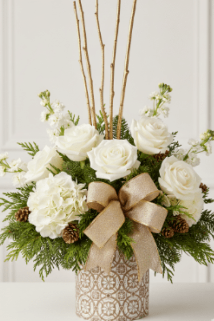 Gold &amp; White Noel Bouquet - I noticed you uploaded several images in your last request, but the image you uploaded just before this one (labeled image_0e8e99.png in the list) is a beautiful white, gold, and green arrangement in a patterned cylinder vase.  Assuming you are referring to this centerpiece:   Gold &amp; White Noel Bouquet Description Radiate sophisticated winter charm with our Gold &amp; White Noel Bouquet. This elegant, high-impact design features classic white roses and full white hydrangeas, paired with fragrant stock flowers and delicate white waxflower. The arrangement is beautifully framed by fresh evergreen boughs and accented with natural pinecones and striking gold curly willow branches. All elements are housed in a chic white and gold patterned cylinder vase, tied with a luxurious champagne satin ribbon. This piece is the perfect Christmas floral gift, a stunning holiday centerpiece for a mantle, or an impressive addition to your winter wedding decor. Available for easy online ordering and local flower delivery!
