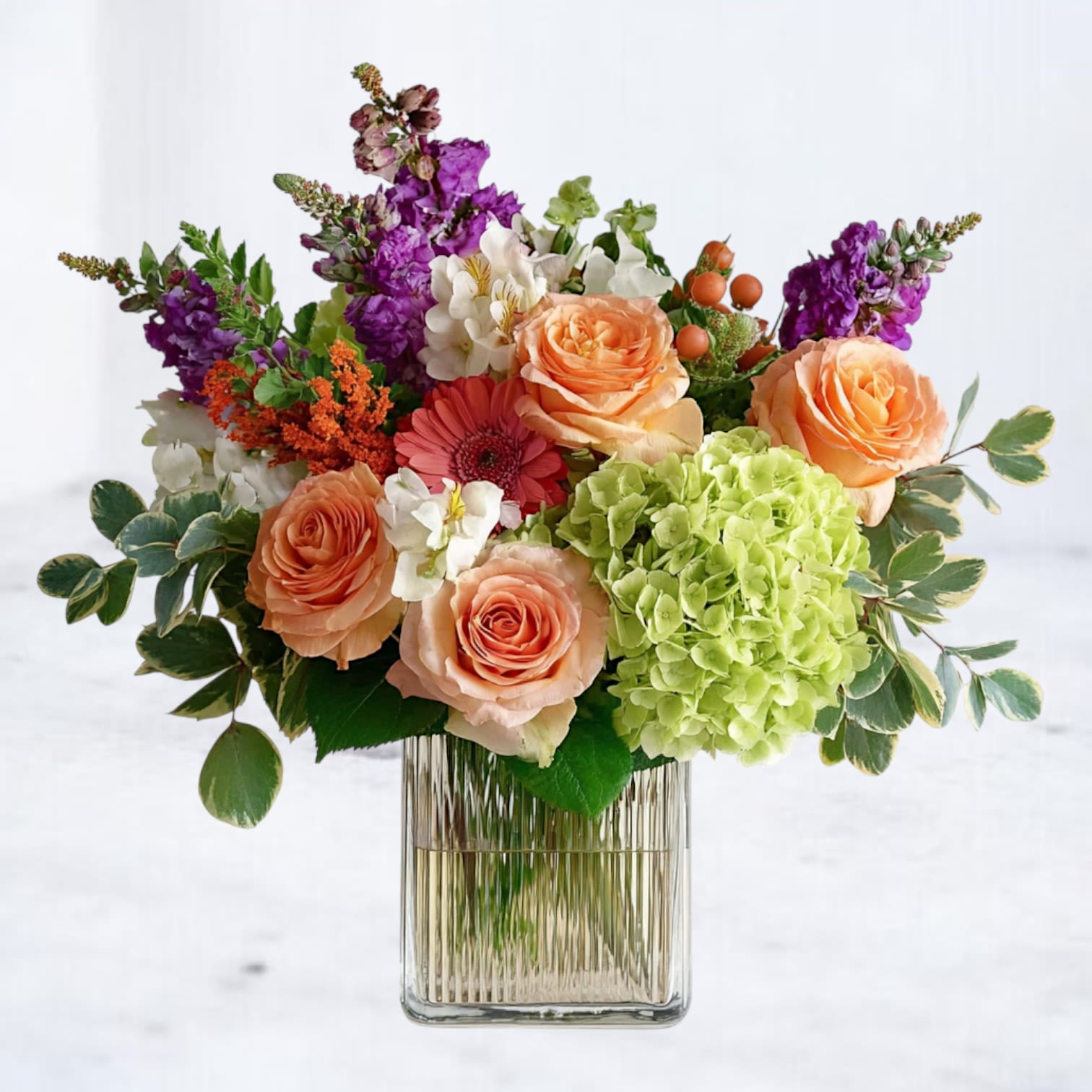 Verdant Jewel Bouquet - Bright, bold, and brimming with charm, the Verdant Jewel Bouquet celebrates nature’s vibrancy with a stunning mix of green hydrangea, peach roses, coral gerbera, violet stock, orange accent blooms, and fresh foliage. Arranged in a modern glass vase, this design blends rich jewel tones with soft seasonal hues, making it perfect for birthdays, celebrations, or simply sending joy just because.  Occasions: Everyday gifting, birthdays, thank-you gestures, or housewarmings.  Available for same-day delivery in Magnolia, The Woodlands, Spring, Montgomery, and surrounding areas.