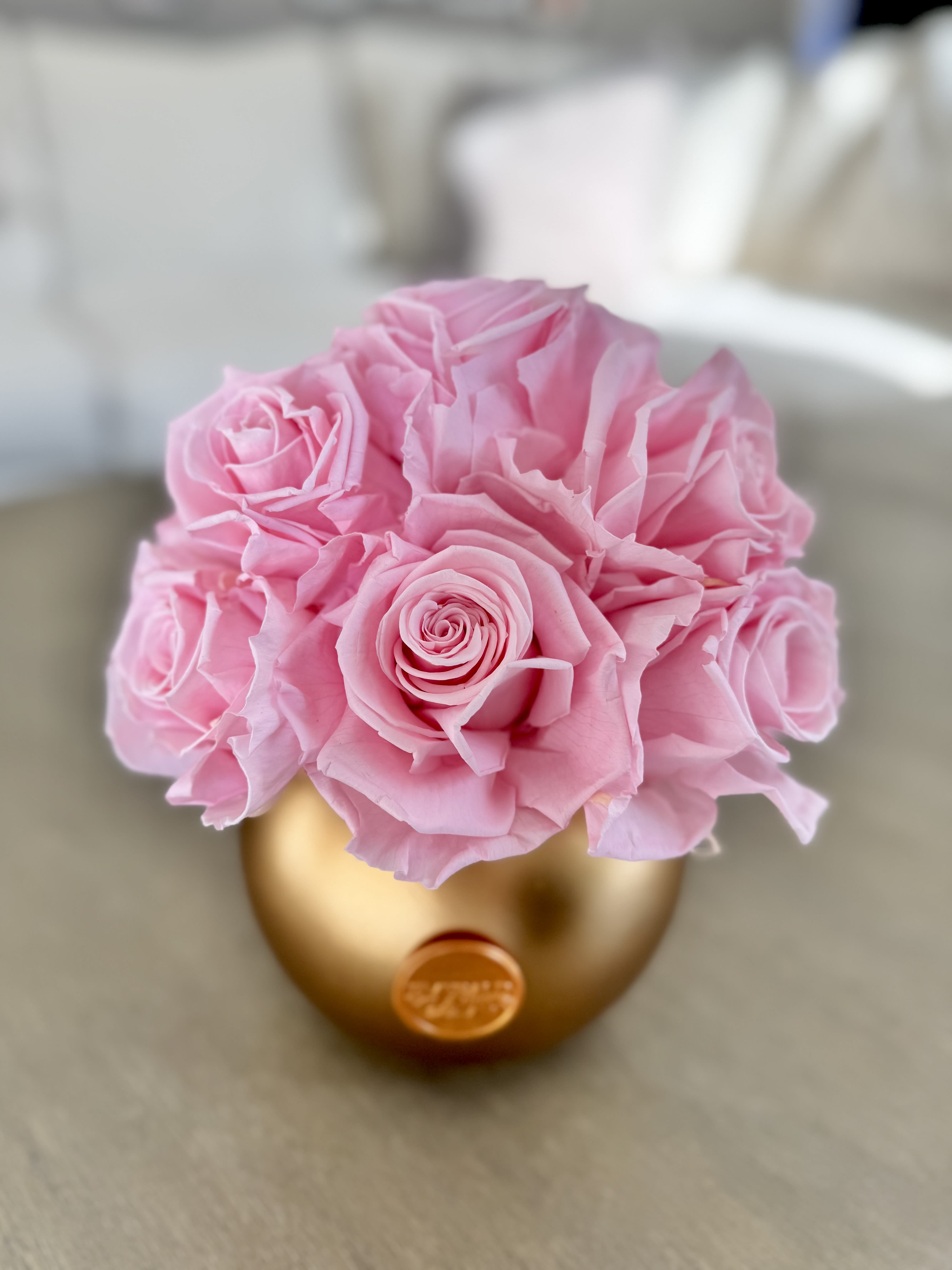 Eternelle Blush - Gold Luxe Orbe - Soft, romantic, and timeless, the Eternelle Blush - Gold Luxe Orbe showcases exquisitely a dozen preserved blush roses in a stunning gold orbe vase. This elegant arrangement embodies grace and sophistication, making it the perfect statement piece or heartfelt gift for any occasion. Its compact yet luxurious design makes it ideal for a desk, bedside table, or any space in need of a touch of beauty and elegance.  Dimensions: 8in W x 9in H  Care Tips: To preserve the beauty of your Eternelle arrangement, keep it in a cool, dry place away from direct sunlight, humidity, and heat sources. No watering or maintenance is required—simply enjoy its everlasting elegance. Avoid touching the roses frequently to maintain their delicate texture, and use a soft brush or gentle air duster to remove any dust from the petals or vase. With proper care, your arrangement will remain a stunning display of luxury for years to come.  Availability: Each Eternelle arrangement is handcrafted with the utmost care. If this arrangement is marked SOLD OUT, you can place an order to reserve yours, and we will provide the earliest available delivery date. Please allow approximately one week for restocking and fulfillment. Thank you for your patience as we create your exquisite arrangement.