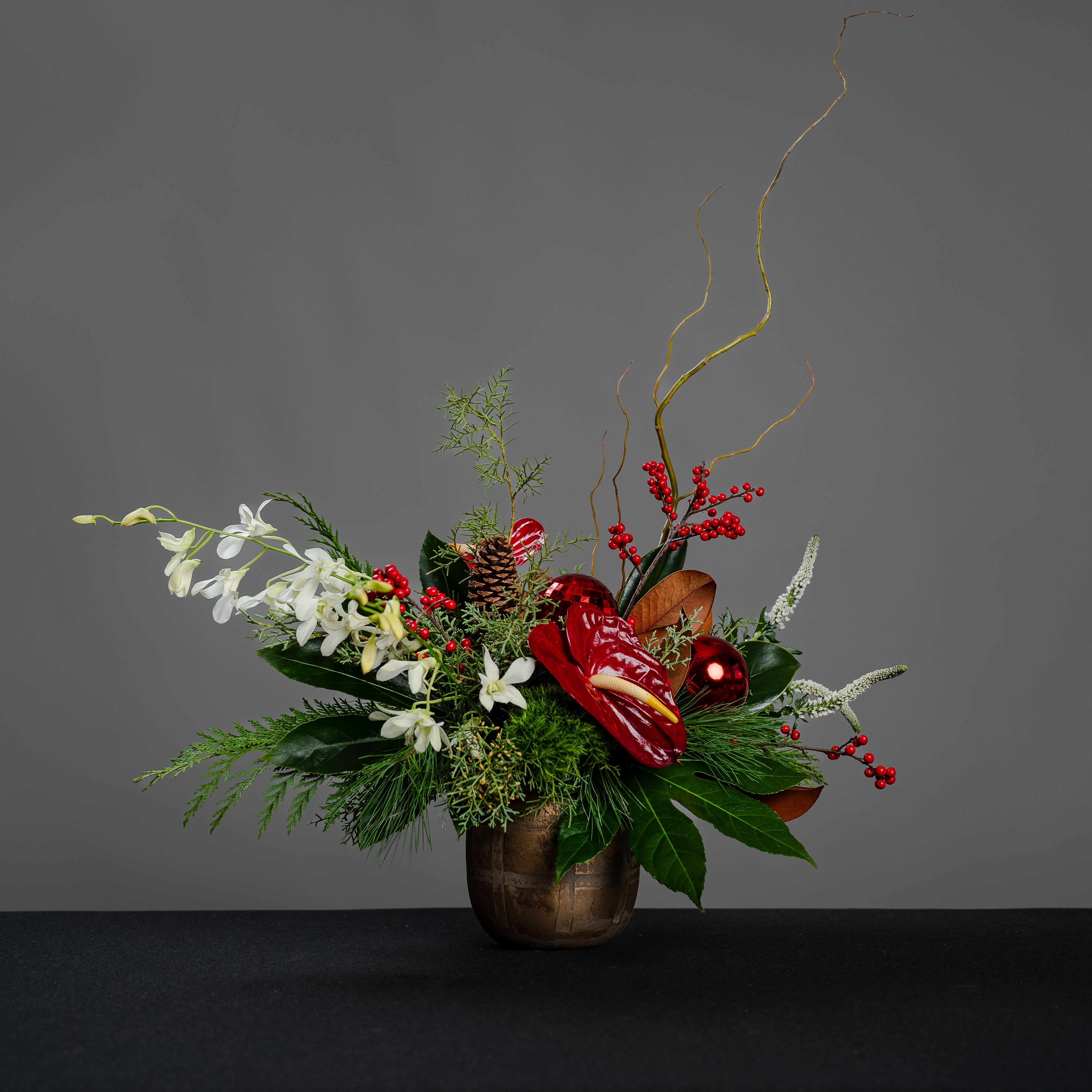 Rudolph - Gold vase filled with anthurium, dendrobium orchids, veronica and berries, accented with a variety of greenery, natural branches, pine cones, and natural branches. Approximate size 22&quot; wide and 20&quot; tall.
