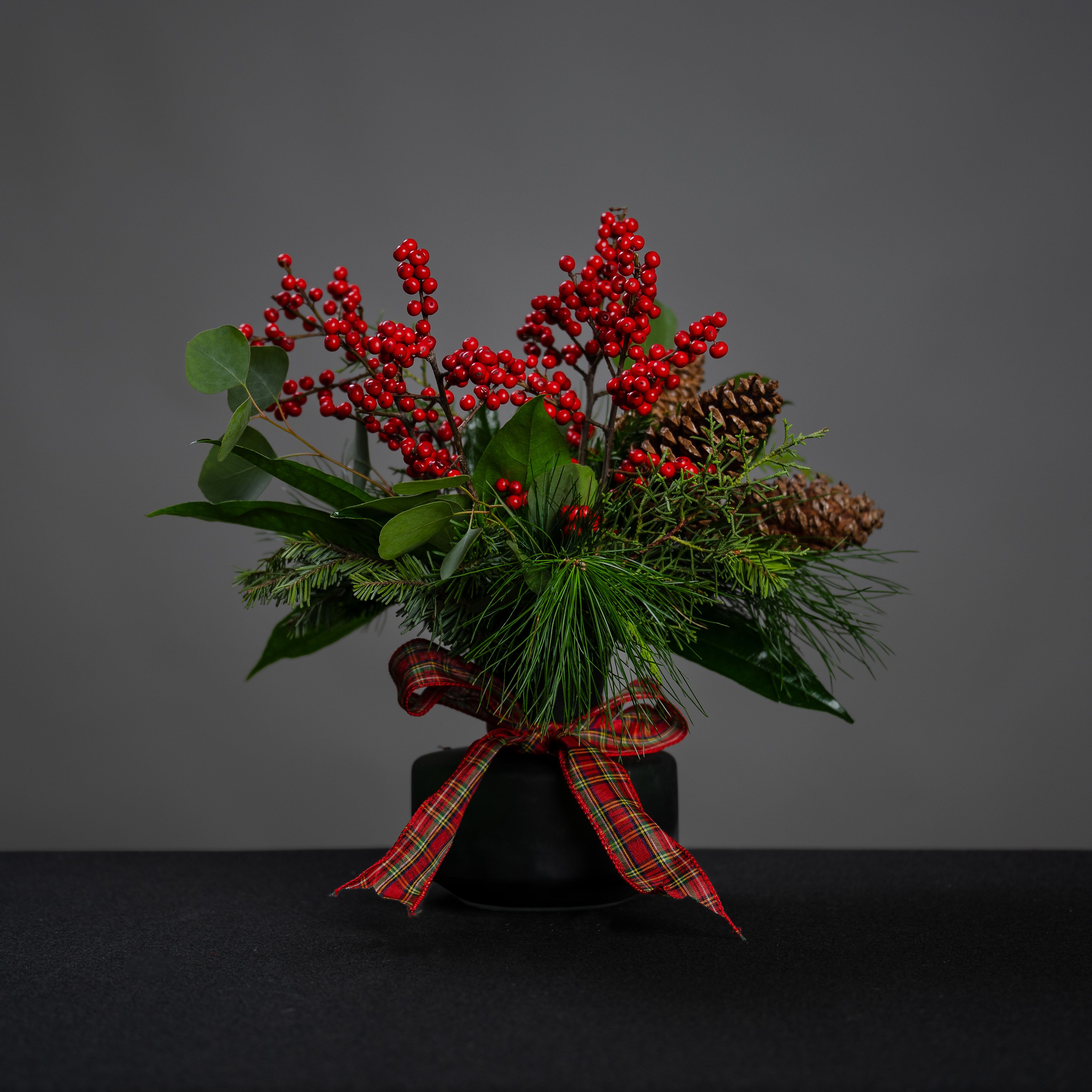 Plaid Christmas - Gorgeous green vase, that's a gift by itself-- but this one is filled with a variety of winter greenery and stems of winterberry, accented with pine cones and a red plaid bow. Approximate size is 17&quot; wide and 14&quot; tall.