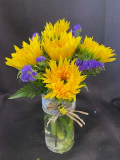 Bee Well - Brighten someones day with this beautiful &amp; whimsical arrangement with Sunflowers, Purple Staicce &amp; seasonal greenery arranged in a glass vase with raffia bow with a bee center.
