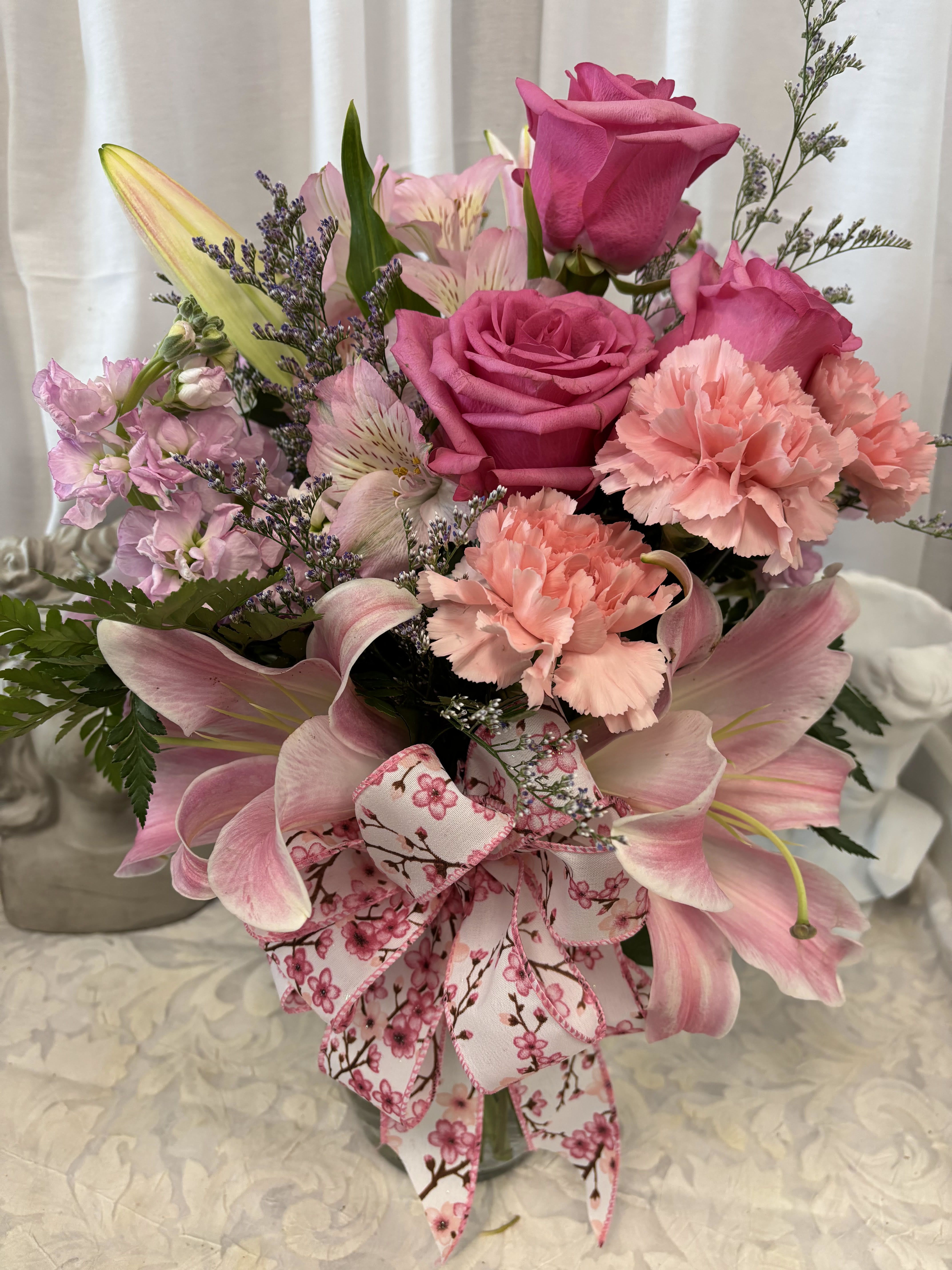 Shades of Pink - Pink, Pink and more pink.  Pink Roses, Lilies, Carnations, Alstromeria and wax flowers with seasonal greenery in a clear vase with a pretty cherry blossom patterned bow