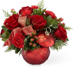 Christmas Magic Bouquet - The keepsake red ceramic ornament ball complete with just enough glitter in a swirled fashion is filled with a beautiful ribbon and the best seasonal greens and red flowers.