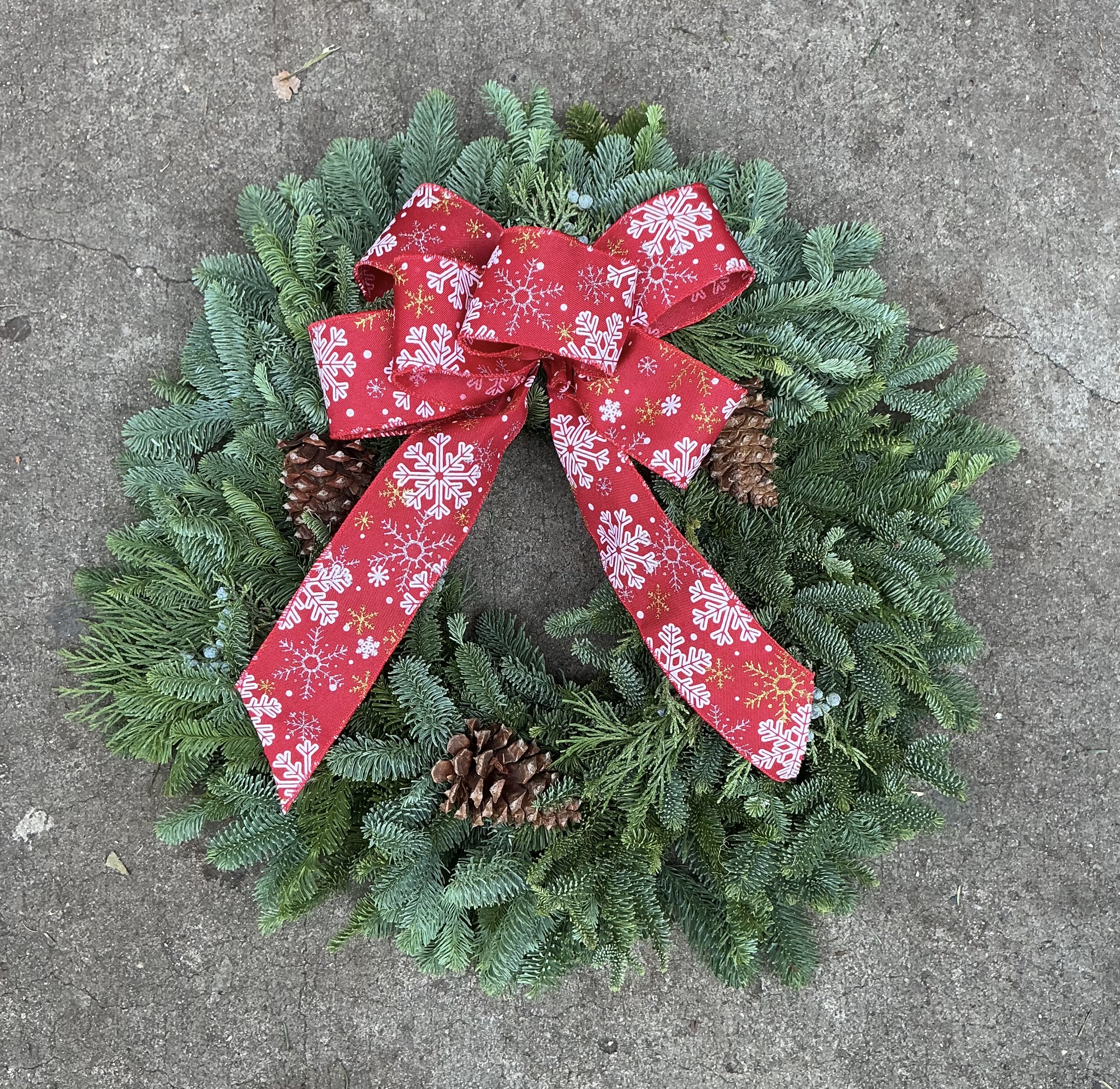 Classic Holiday Pine Wreath  - Make a bold, festive statement this season with our best-selling 20 inch holiday wreath. Crafted with fresh, full evergreens and accented with real pinecones, this wreath brings instant Christmas warmth to any door. The bright red snowflake ribbon adds the perfect pop of color that customers love for holiday photos, gifting, and storefront décor.
