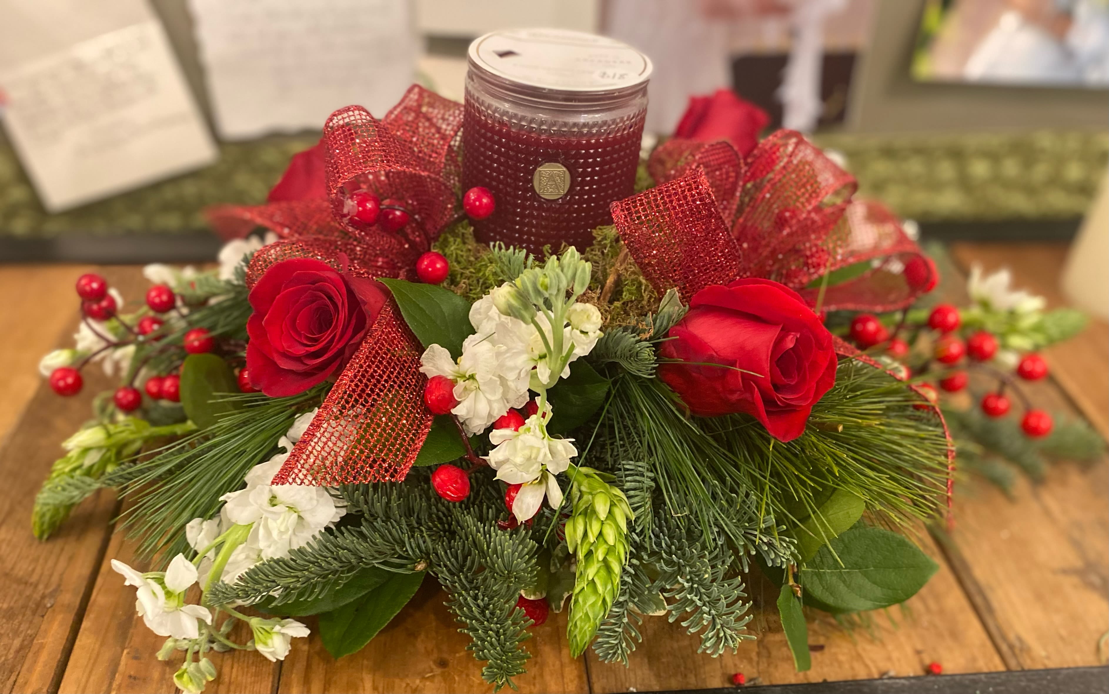 The Smell of Christmas - This beautiful centerpiece is sure to brighten anyones home this Holiday season! The Smell of Christmas candle is surrounded by beautiful red and white flowers and lush winter greenery.