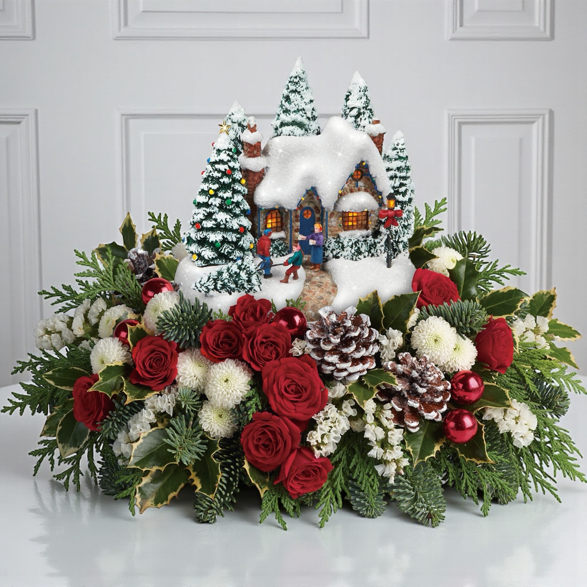 Thomas Kinkade's a Christmas Welcome Bouquet - Here's something to be excited&nbsp;about! This charming, hand-painted Thomas Kinkade collectible is nestled in festive red roses and winter greens for an unforgettable gift.&nbsp;   This festive Thomas Kinkade's Christmas arrangement features red roses, red carnations, miniature red carnations, white pine, seeded eucalyptus and lemon leaf. Delivered with Teleflora's Thomas Kinkade's Christmas &quot;A Christmas Welcome&quot; Keepsake.  Orientation: All-Around&nbsp;  Sizes:  Standard: 10 3/4&quot; H by 15 1/2&quot;W&nbsp;  Deluxe:&nbsp;10 3/4&quot; H by 16 1/2&quot; W  Premium: 10 3/4&quot; H by 18&quot; W     