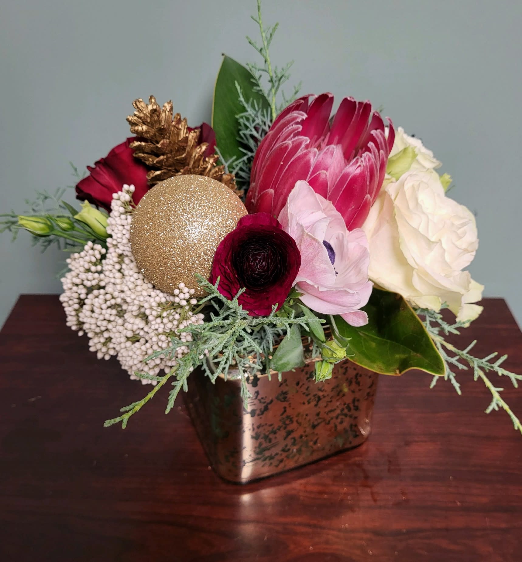 Vintage Yuletide - As our newest design, this vintage-style unique and exquisite arrangement will be filled with Designer chosen blooms and ornaments artfully arranged in a striking 5 x 5 mercury glass gold or silver square glass vase.   Please specify gold or silver in the Special Instructions section.  If no selection is made Designer will choose.  