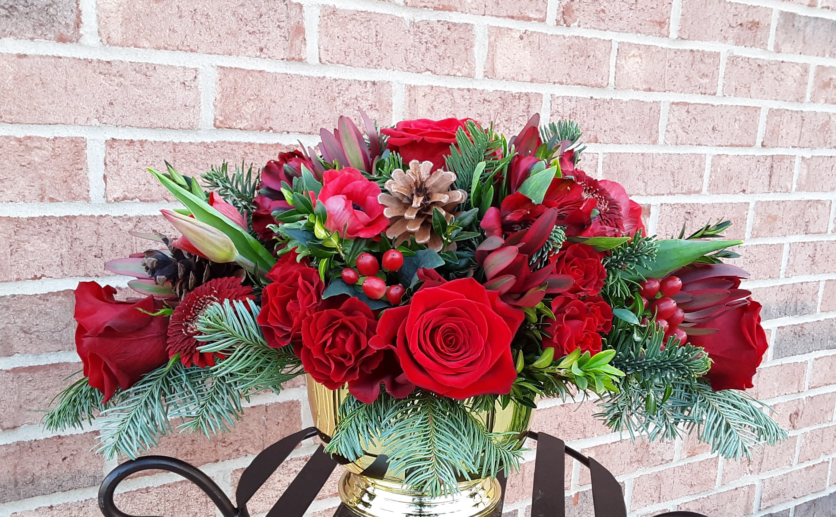 Magnificent &amp; Marvelous - This incredible mixed red floral centerpiece is artfully arranged and nestled in mixed pines and greens in a gold pedestal dish.  STANDARD PRICE RANGE represents a ROUND arrangement and is approximately 14" in diameter. THE DELUXE OPTION would be an long style centerpiece approx 24"in length and 14" wide.  Chose based on recipients table size.  Also accents and dish can be gold or silver. Specify your choice in the Special Instructions section.  If no choice is indicated, Designer will choose.