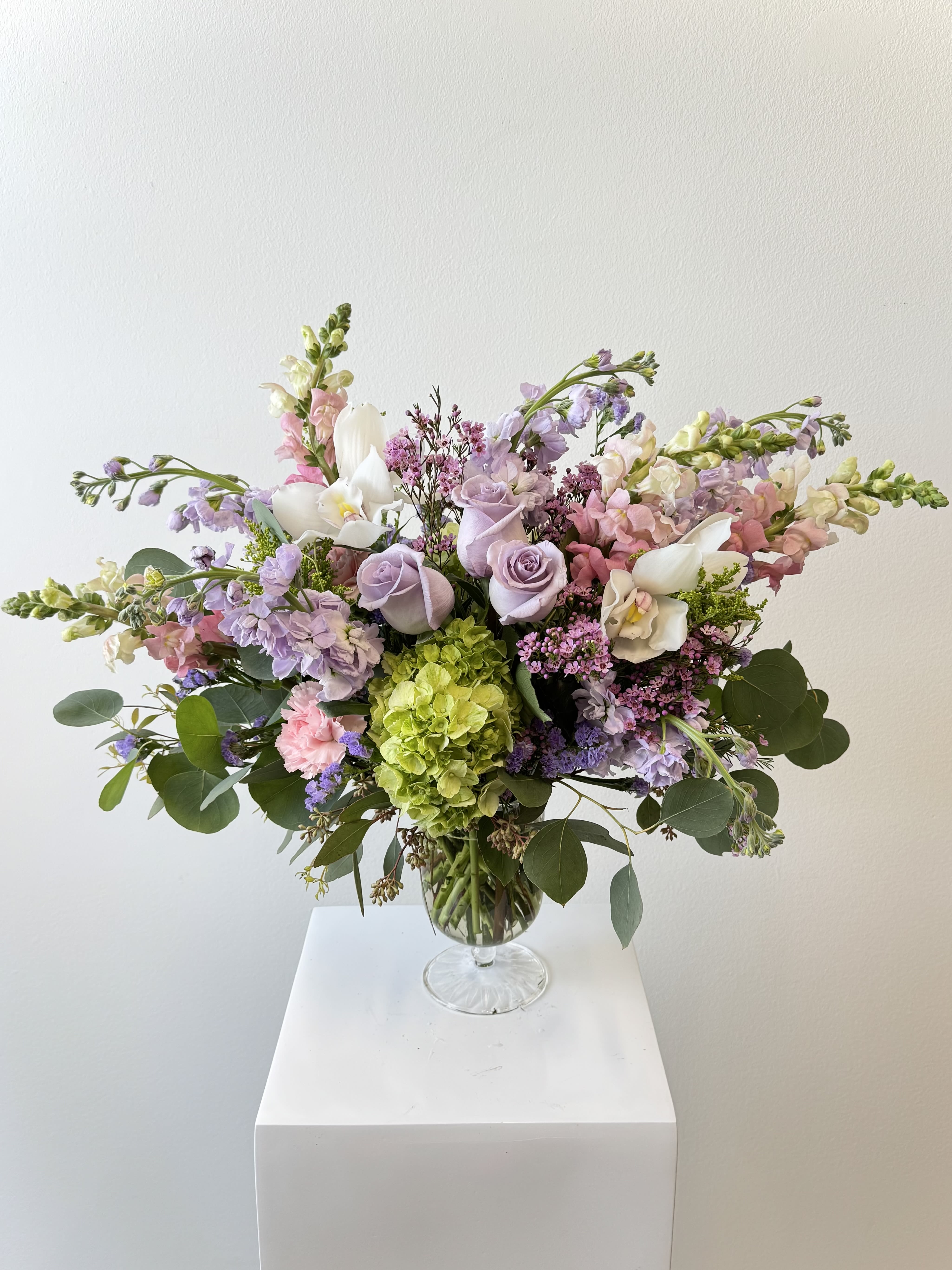 Wild About You - Fall wildly in love with the &quot;Wild About You&quot; bouquet: an enchanting blend of elegant whites and soft lavender hues that screams romance. Lush green hydrangeas create a dreamy, full base, perfectly paired with majestic white cymbidium orchids that add exotic sophistication and graceful arches. Fragrant lavender stock fills the air with its calming scent, while tall white snapdragons bring dramatic height and texture. Delicate lavender roses steal the show with their romantic beauty and subtle fragrance, complemented by tiny wax flowers for a whimsical, wildflower touch. Wispy purple statice adds long-lasting color and a meadow-like charm, making this arrangement feel fresh-picked yet luxuriously refined. Hand-designed by expert florists using premium fresh blooms, it’s perfect for anniversaries, &quot;I’m crazy about you&quot; moments, birthdays, housewarmings, or just because. A customer favorite for its romantic lavender-pink palette!  What’s inside:  White cymbidium orchids  Full green hydrangeas  Fragrant lavender stock  Tall white snapdragons  Soft lavender roses  Delicate wax flowers  Purple statice  Same-day delivery available in Orange County. Keywords: lavender and white bouquet, romantic flower delivery, white cymbidium orchid arrangement, lavender rose bouquet, wildflower style flowers, anniversary bouquet, luxury pastel flowers, best-selling romantic bouquet, purple and white flowers.  Say “I’m wild about you” in the most beautiful way – order now!