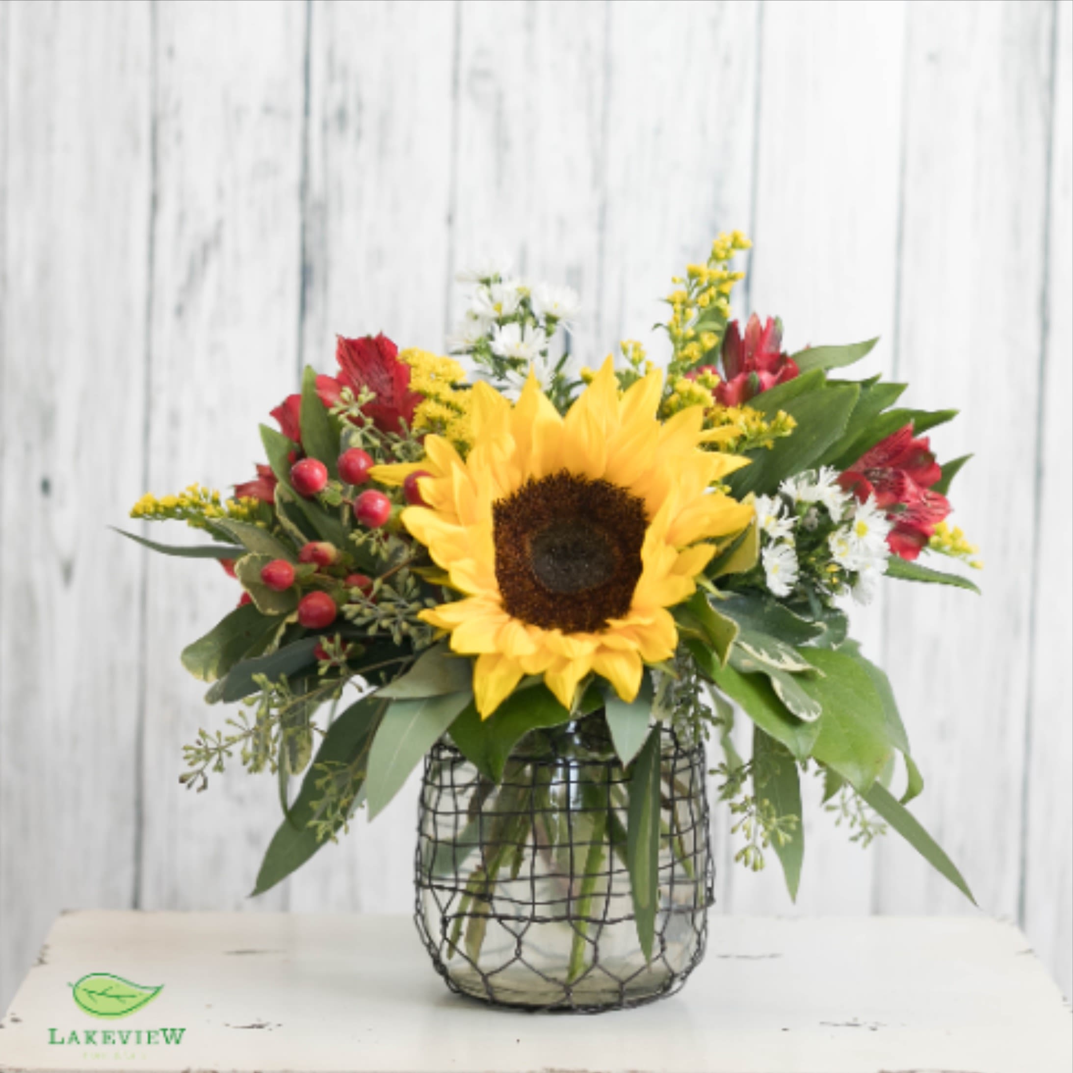 Pioneer - Sweet and petite!  This arrangement features a bright sunflower paired with red blooms and berries in a wire wrapped vase for a countryside feel.  Approx. 10&quot;H x 8&quot;W