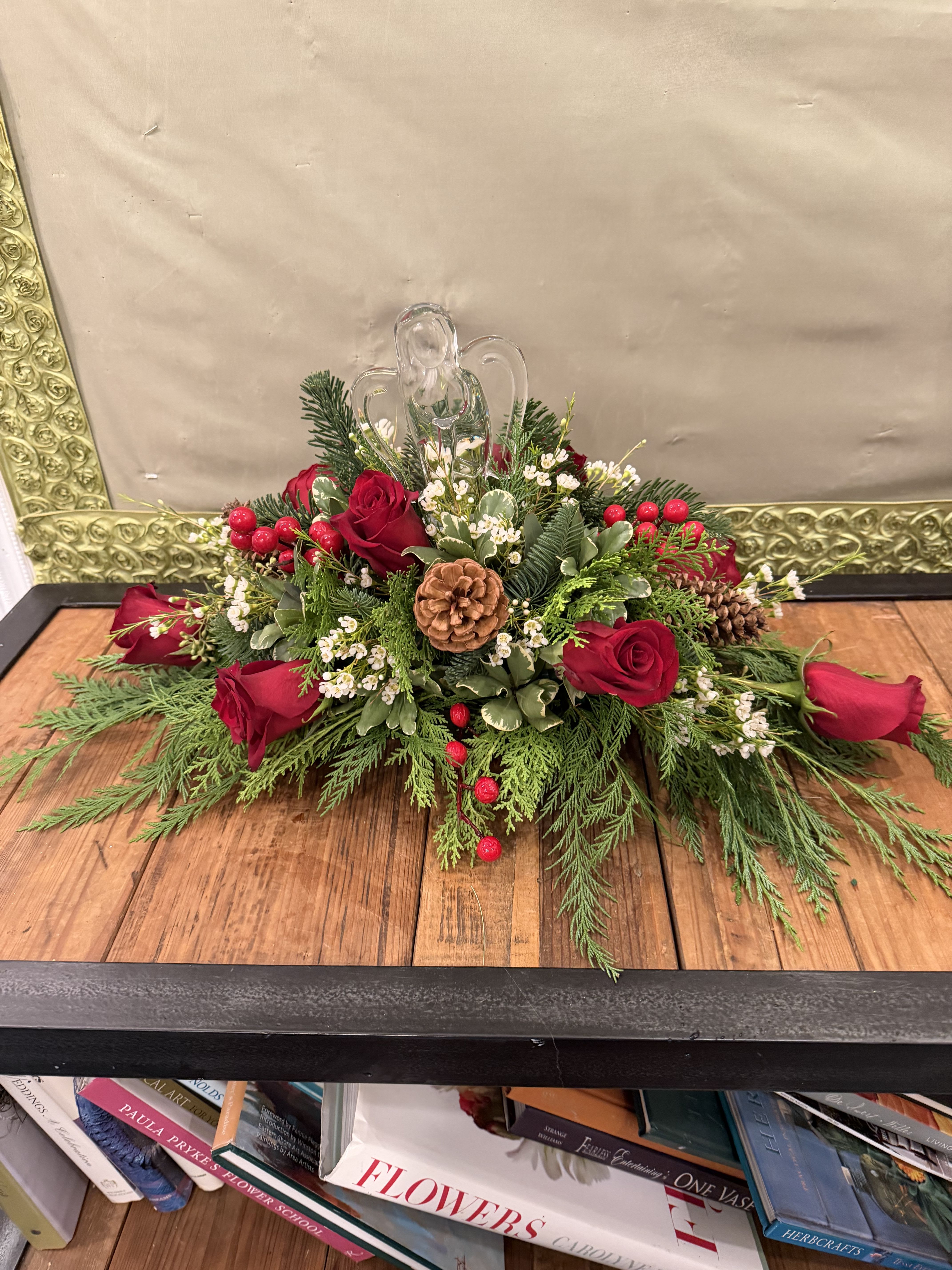 Christmas On High Bouquet - A beautiful crystal angel is the center of this joyful bouquet. Beautiful red blooms and Christas greens make this a perfect centerpiece for any holiday gathering.