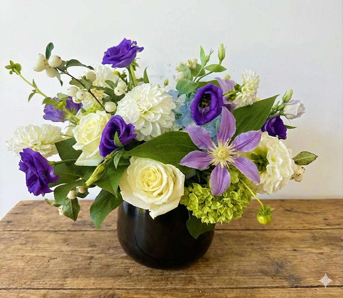 Midnight Garden - Striking yet serene, Midnight Garden is a moody blend of violet lisianthus, lavender clematis, white roses, dahlias, hydrangeas, and snowberries. The cool color palette pops beautifully against lush greens and a modern matte black vase, making it a standout gift or centerpiece for lovers of deep, elegant hues.  Details: 	•	Flowers: lisianthus, clematis, white roses, dahlias, hydrangeas, snowberries 	•	Arranged in a black ceramic container 	•	Approx. size: 10-11” wide 	•	Ideal for occasions where color and contrast shine