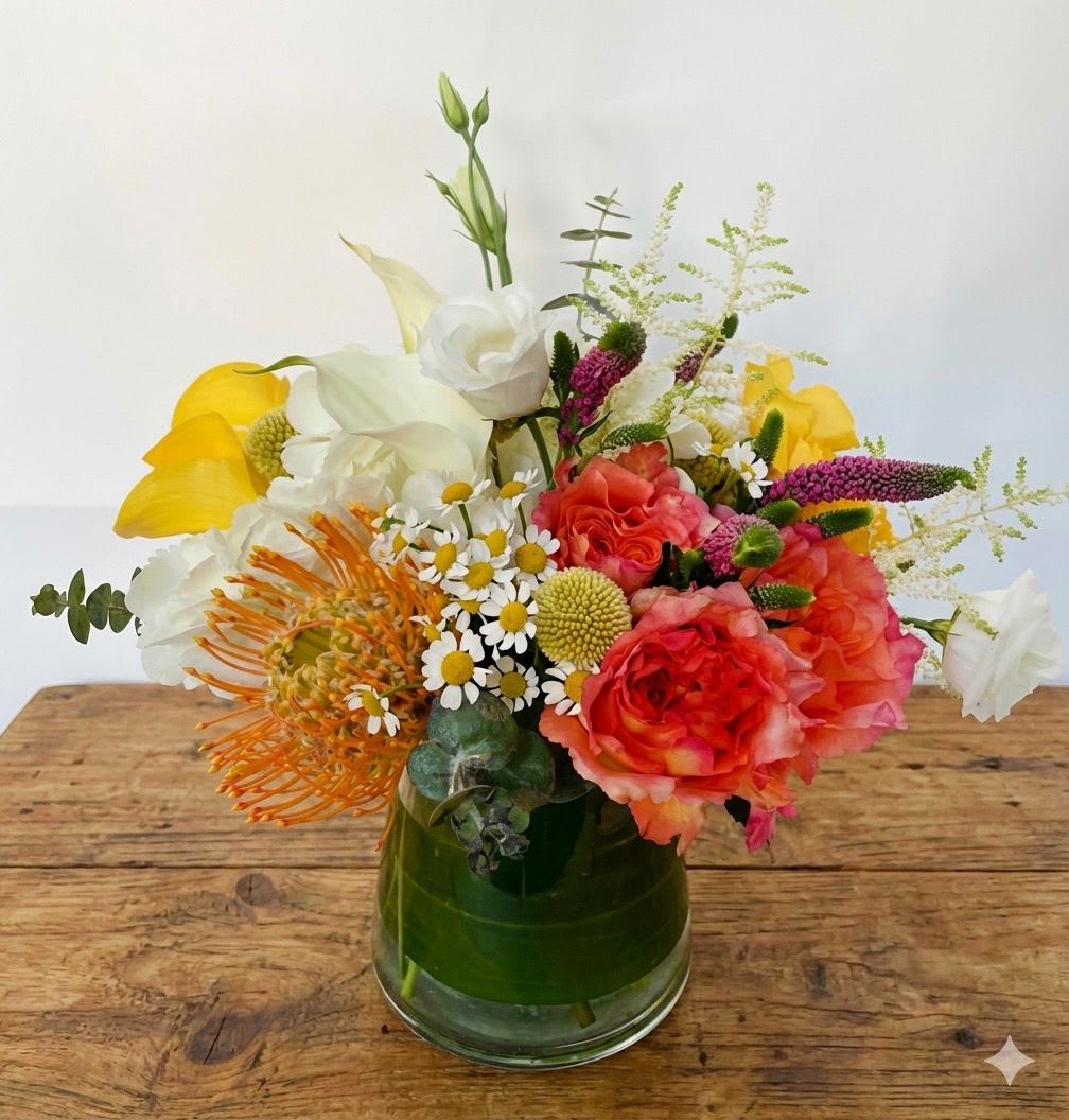 Harvest  - Our Harvest floral design reminds us of new beginnings and trying new things. This colorful and cheerful vase arrangement features a little bit of everything, combining classic with modern florals. Classic white calla lilies and white hydrangeas are complemented by tropical pincushion and craspedia (or Billy balls), Veronica flowers, and free spirit roses, among other flowers. This flower arrangement is presented in a simply and elegant pinched glass vase, with a green leaf wrapped inside for an extra special touch. Standard size pictured. Larger sizes available. Flowers and vase may vary based on availability.