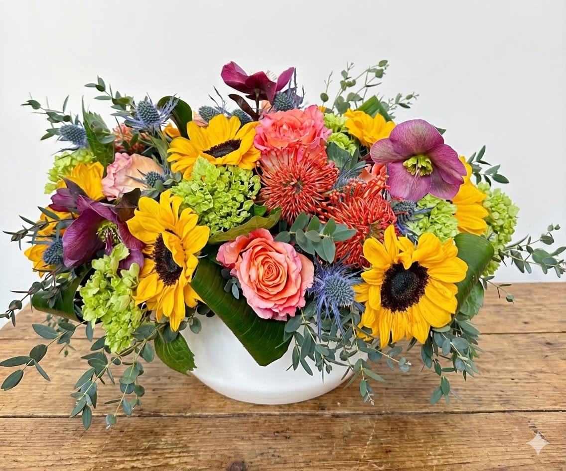 Sunny Side - This arrangement includes sunflowers, green hydrangeas, pincushions, free spirit roses, burgundy hellebore and assorted greens. The arrangement is presented in a very modern white ceramic container. 