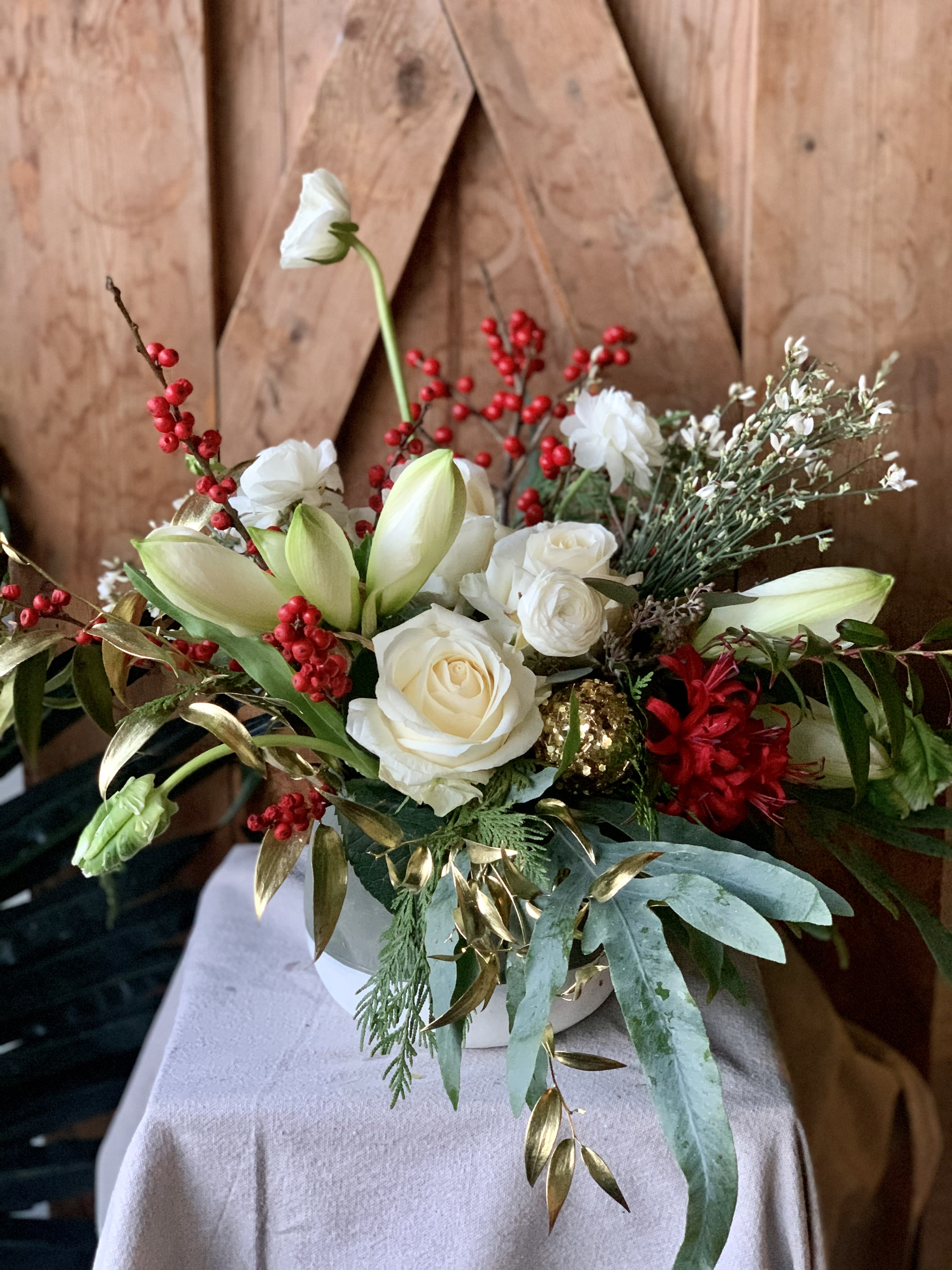 'Tis the Season - Classic white and red holiday arrangement with hints of gold baubles and foliage.  Lots of berries, evergreen, amaryllis, ranunculus, parrot tulips and white roses for the perfect seasonal statement.  One of our all time favorites!