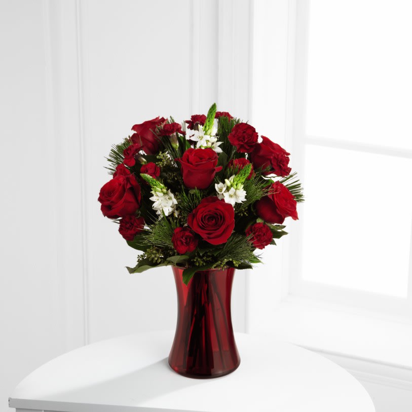 The Holiday Romance Bouquet (RED VASE SOLD OUT) We will use a clear vase with red bow. - The Holiday Romance Bouquet bristles with the passion and wonder of the Valentine season. Rich red roses and burgundy mini carnations accented with the snowy white blooms wax flower and and lush greens will easily sweep them off their feet. Arranged in a ruby red clear glass vase, this bouquet conveys your most heartfelt holiday wishes.   