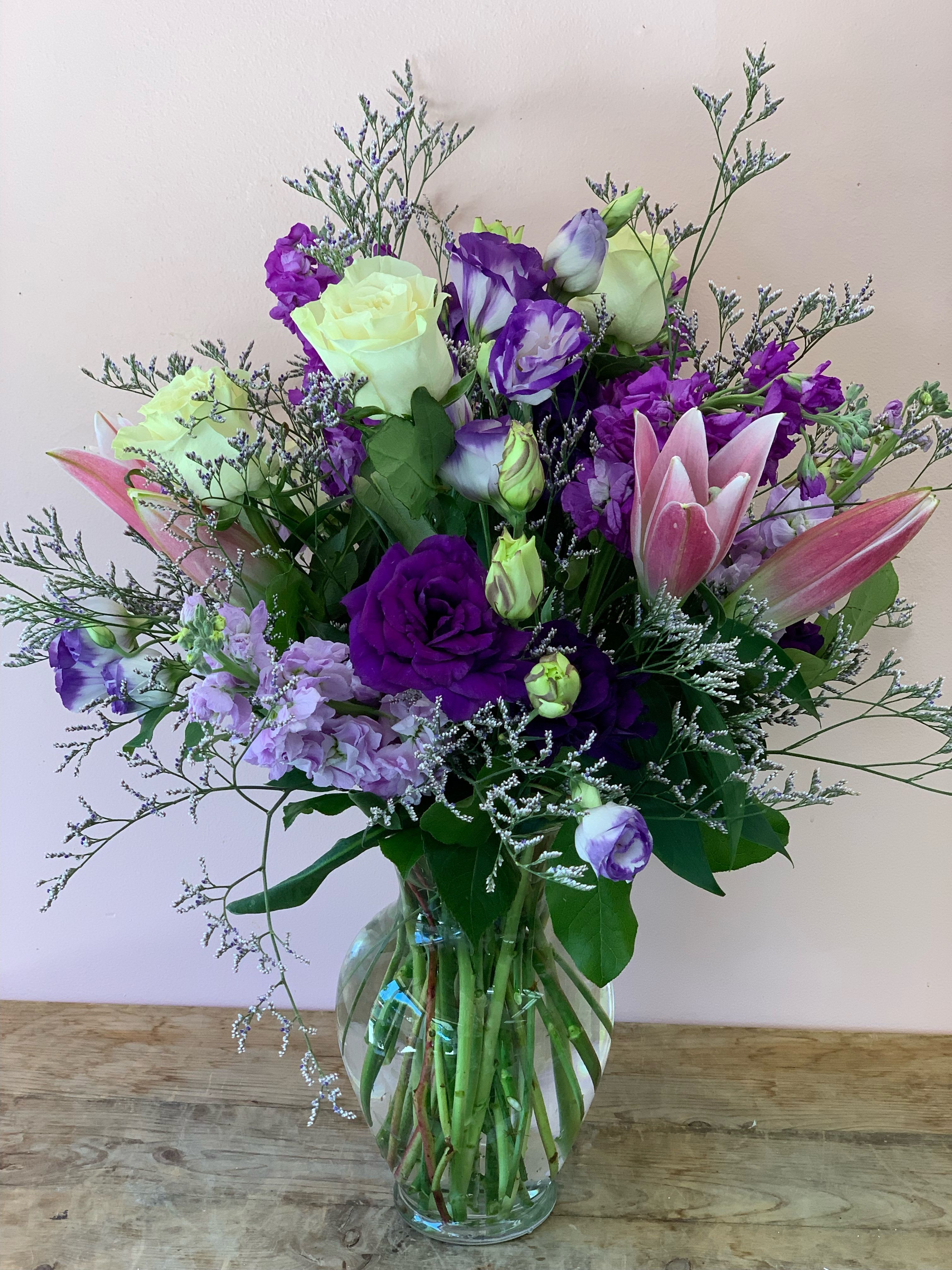 Purple Spotted Queen Flower Arrangement by Fillmore Florist San Francisco - When in doubt about which flowers to buy, we recommend you go with one of our a wild and natural flower designs. Purple Spotted Queen Flower Arrangement is a beautiful bouquet that emits elegance and class from every direction. This delightful bouquet of fresh flowers is made with Lilies, Lisianthus , white Roses, light purple Stocks, with Misty Blue in a clear glass vase. Rest assured Fillmore Florist is your efficient and reliable San Francisco flower delivery service, where your flowers are delivered straight to your front door with our pleasure!  Approximate Dimensions: 15” H x 10” W 