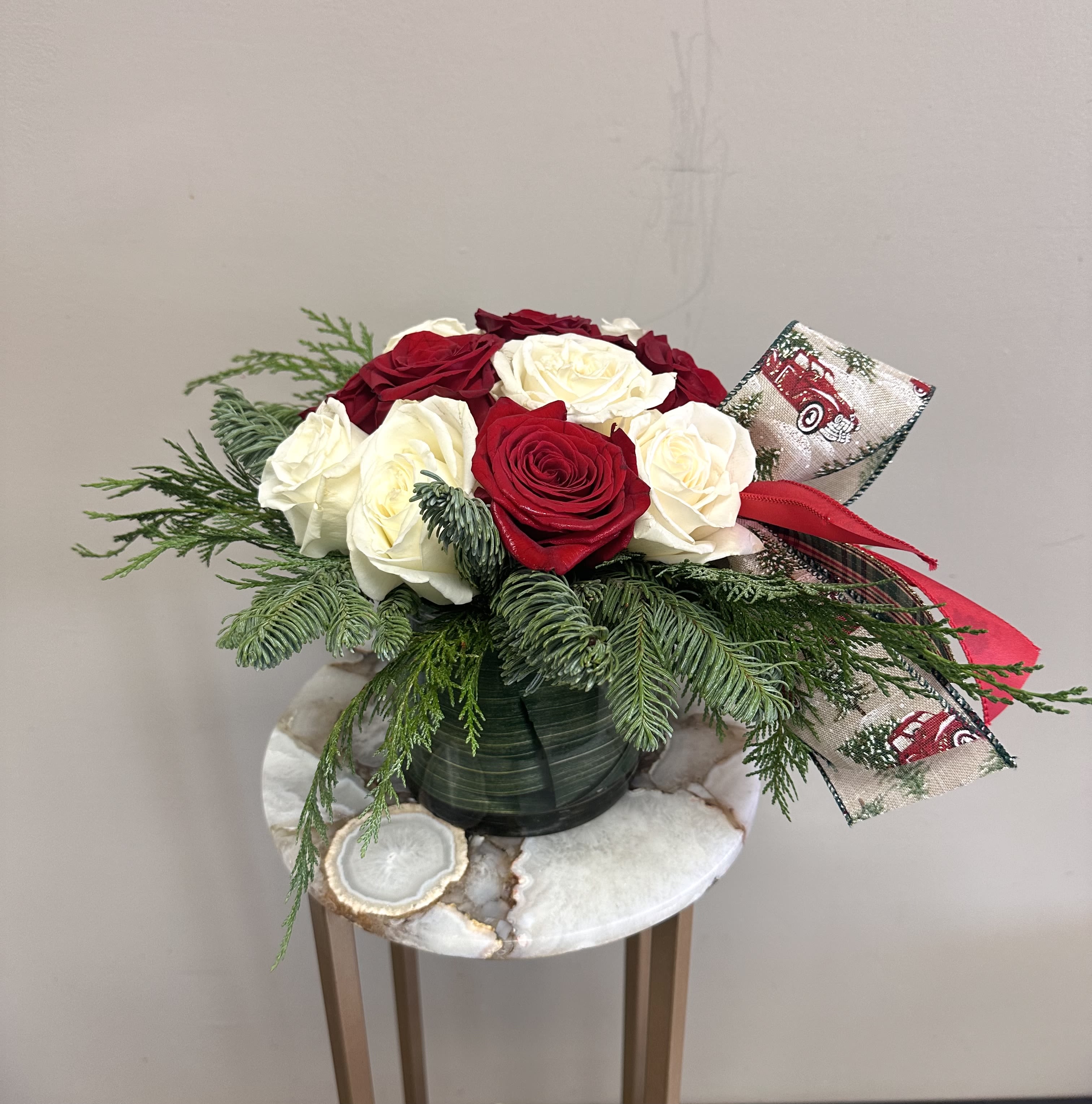 Peppermint Short Dozen - A short and modern styled red and white rose arrangement with holiday greenery and a festive ribbon. 