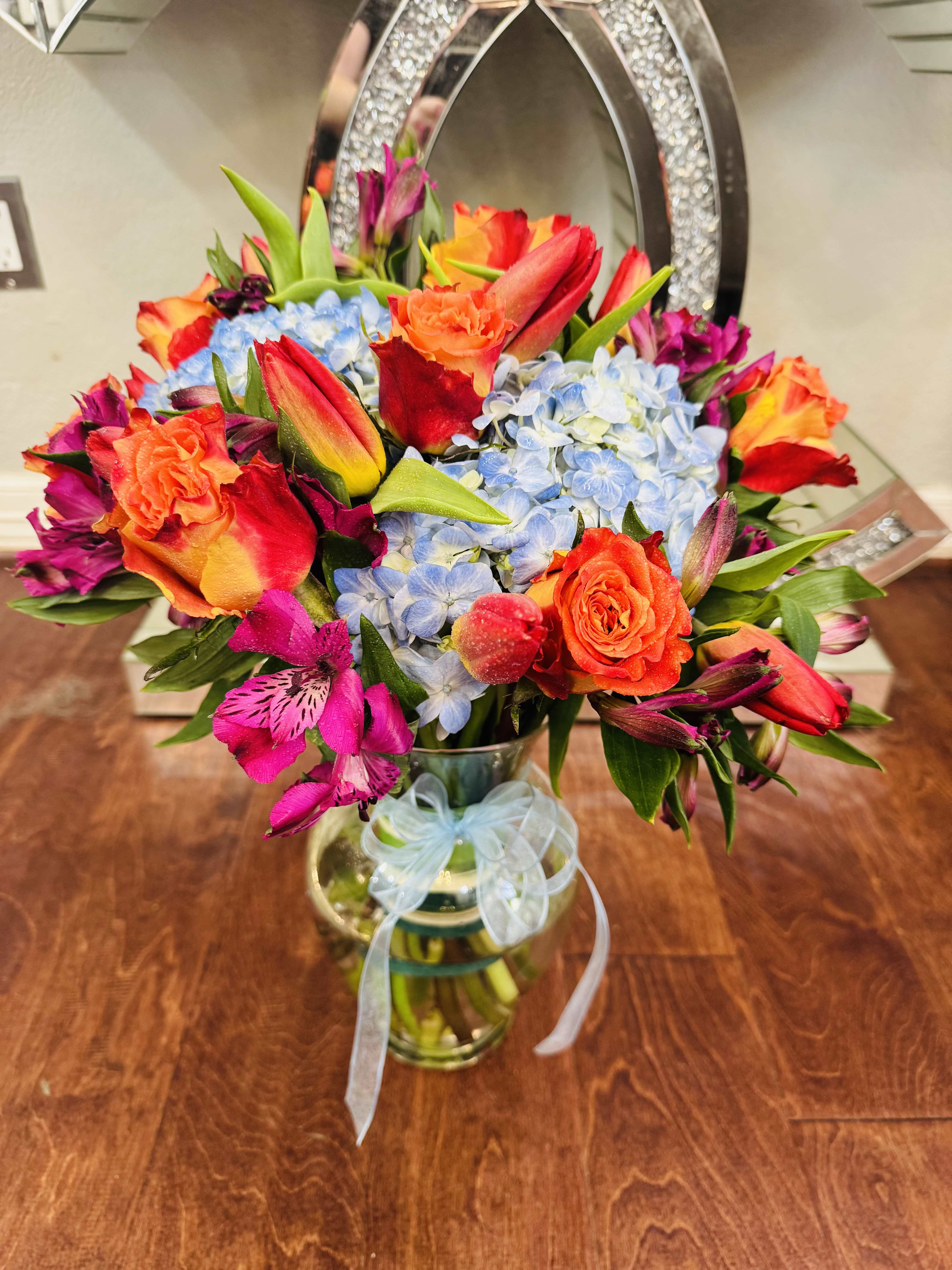 Evening Bloom - A bouquet with orange tulips, orange roses, blue hydrangeas, and pink asters is a stunning mix of warmth brightness, and romantic whimsy. This bouquet is a radiant dance of color and emotion, where charm bloom in perfect harmony. This arrangement feels like a sunset garden full of emotion- passionate, poetic, and beautifully unforgettable. 