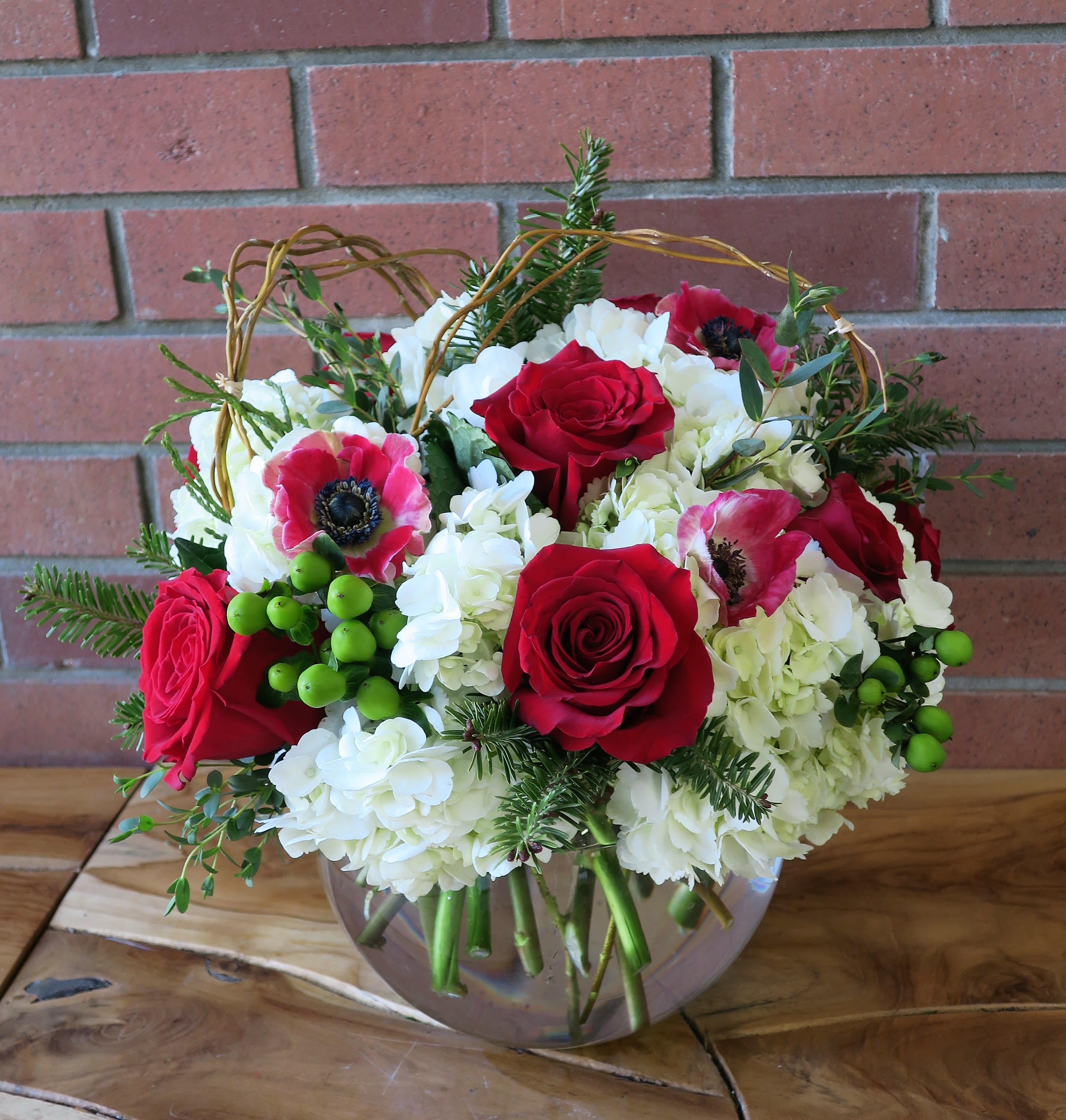 Christmastime  - Bubble bowl filled with fluffy white hydrangeas, red roses, red anemones, green hypericum berries, Christmas greens and branches.
