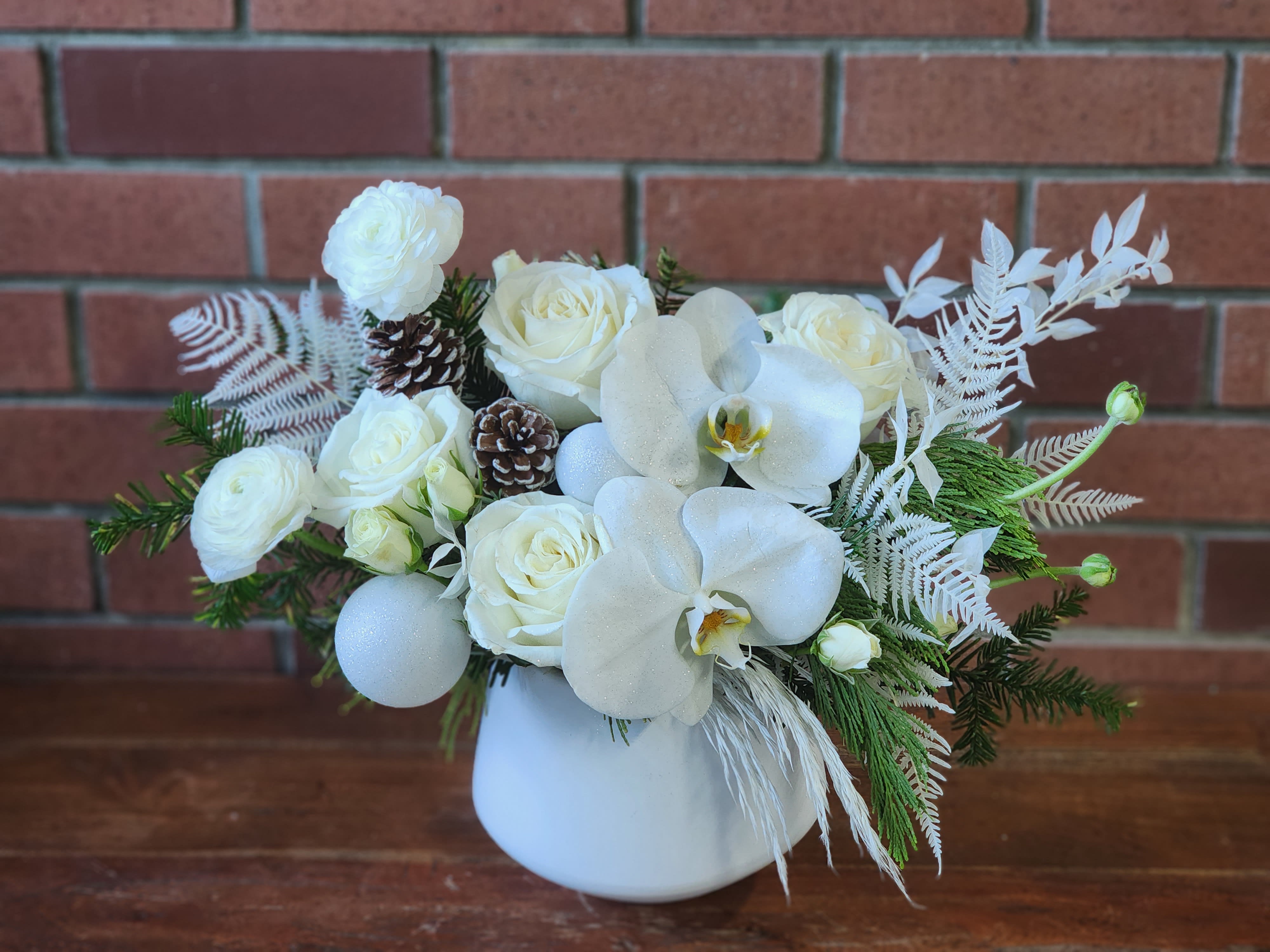 Heavenly Winter Garden Bouquet  - Pure white premium roses, white phal orchids white spray roses preserved bleached greens, frosted pine cones white ornaments with fresh evergreens designed in a high end white ceramic vase 