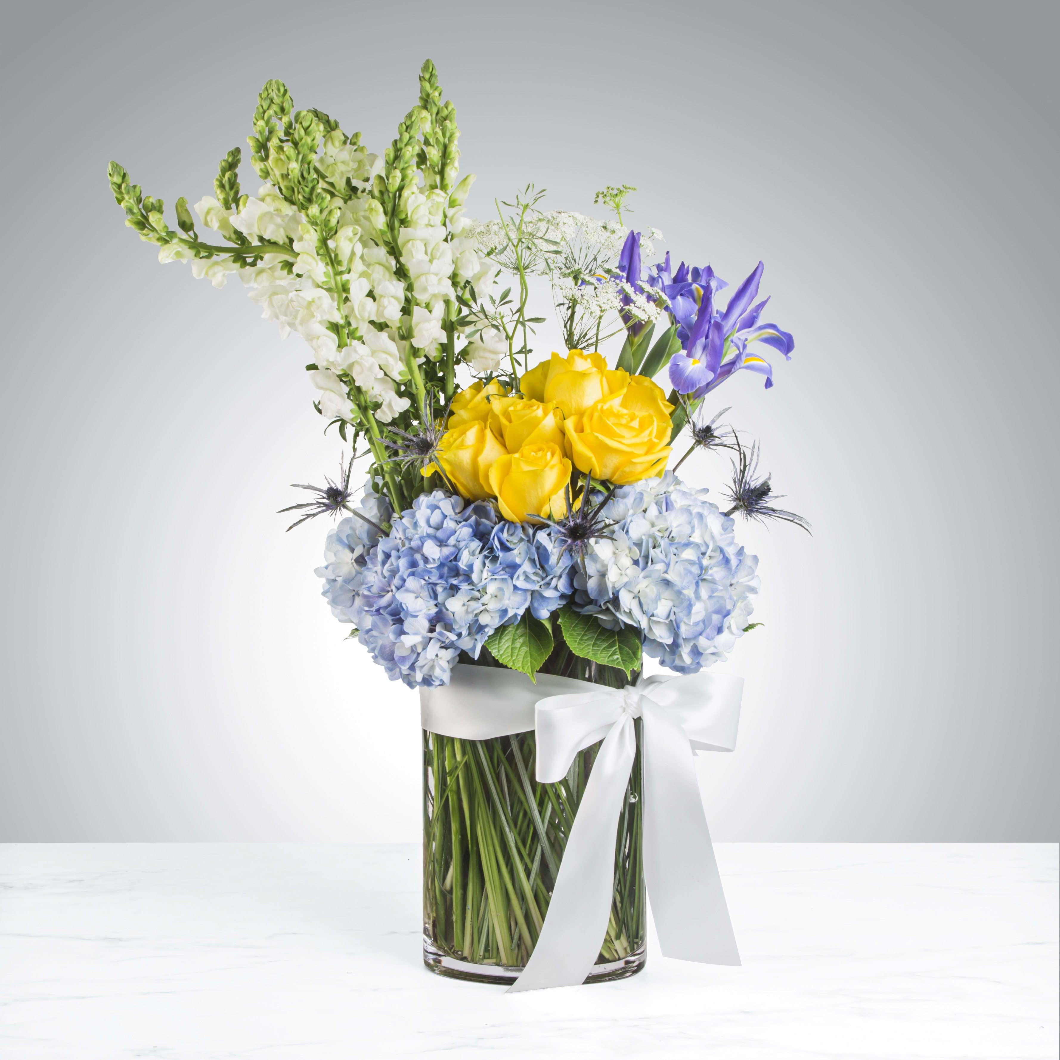 Best in Blue by BloomNation™ - This tall reaching arrangement brings light to any space. A mix of blue and yellow flowers, this arrangement is the perfect way to welcome a new baby, say happy birthday or give thanks.   APPROXIMATE DIMENSIONS 12" W X 20" H