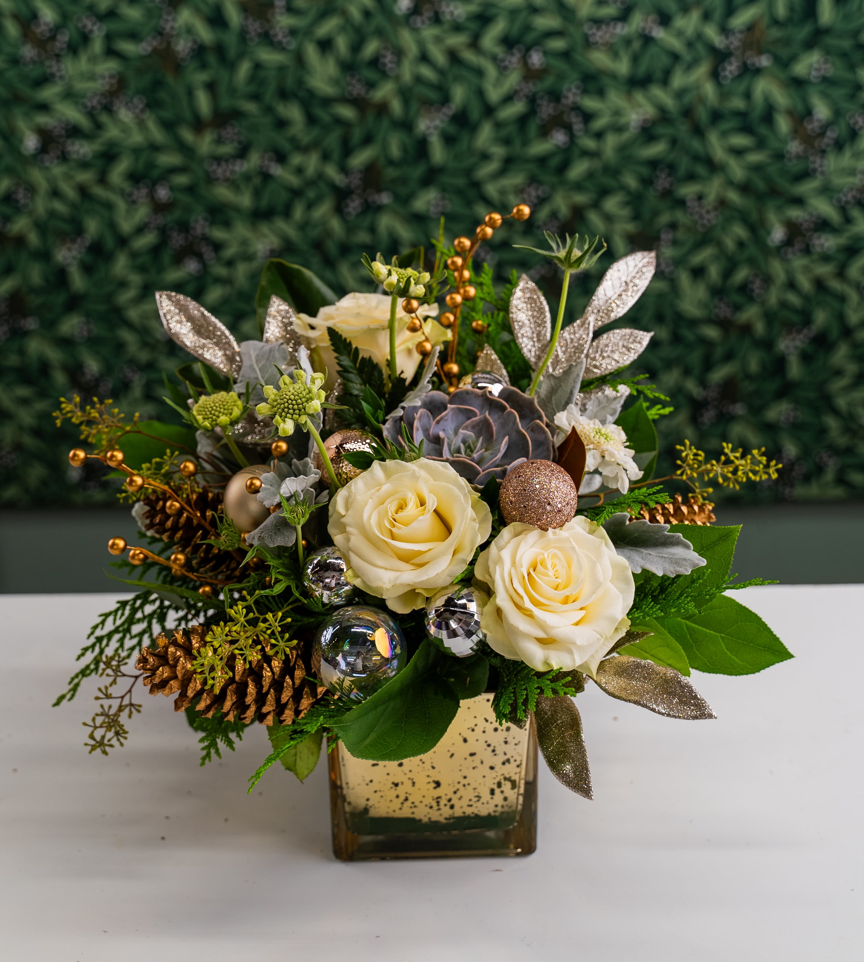 Drop of Gold - Fun composition of wintery evergreen foliage and succulent, white blooms as well as with some sparkly ornaments. Designed in gold mercury glass cube.