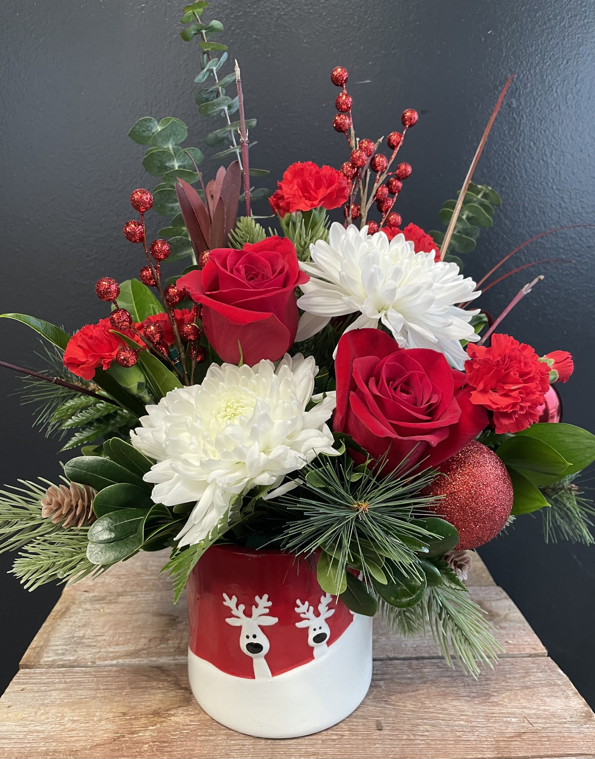 &quot;Run, Run, Rudolph&quot; - The arrangement is crafted in a festive, reindeer container -Interspersed with the red roses, and white cremones. These flowers add a touch of elegance and purity. Their large, full blooms mimic the look of freshly fallen snow, bringing a wintery feel to the arrangement.  