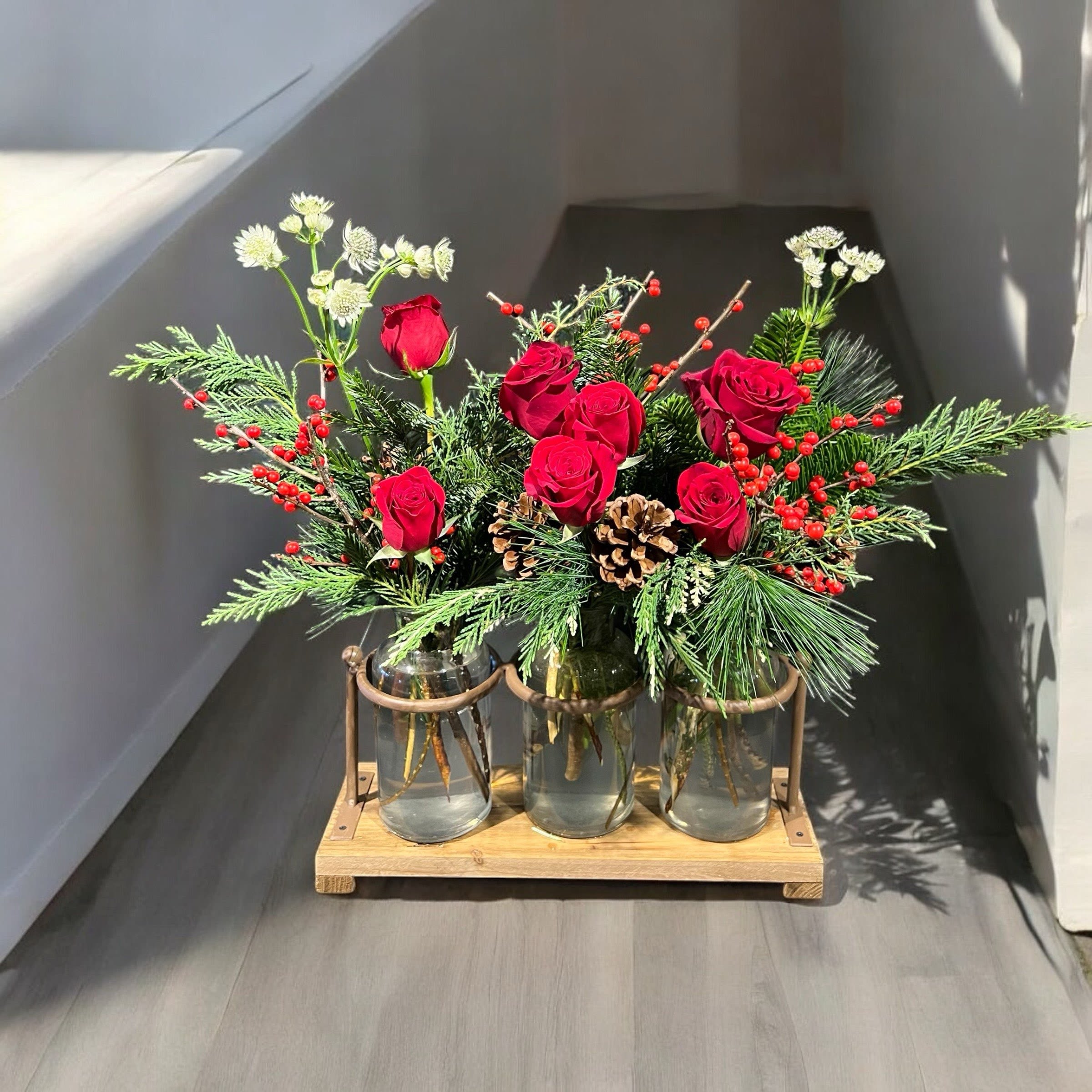 Winter Rose Trio - Wonderful woodsy holiday design in a keepsake trio of apothecary jars in a wood and iron holder.  This creation features a variety of evergreens, red ilex berries, red roses, pine cones and wildflower accents. 