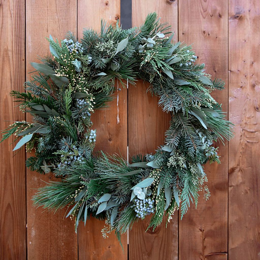 Aromatic Cedar Eucalyptus Holiday Wreath - A lush and naturally elegant wreath made with fresh cedar, fragrant pine, and soft eucalyptus, layered by hand to create a full, textured winter design. The aroma is truly beautiful — the crisp scent of pine, the calming freshness of eucalyptus, and the warm earthiness of cedar blending together like a quiet winter forest. Organic, wild, and timeless, this wreath brings a gentle holiday charm to any door or wall. Perfect for gifting or welcoming guests into your home, it fills your space with the simple, grounding beauty of the season. Our wreaths are 22'-24' in size, made to order for optimal freshness, vibrant, aromatic, and long-lasting. Please allow a minimum of 2 business day notice for delivery availability.