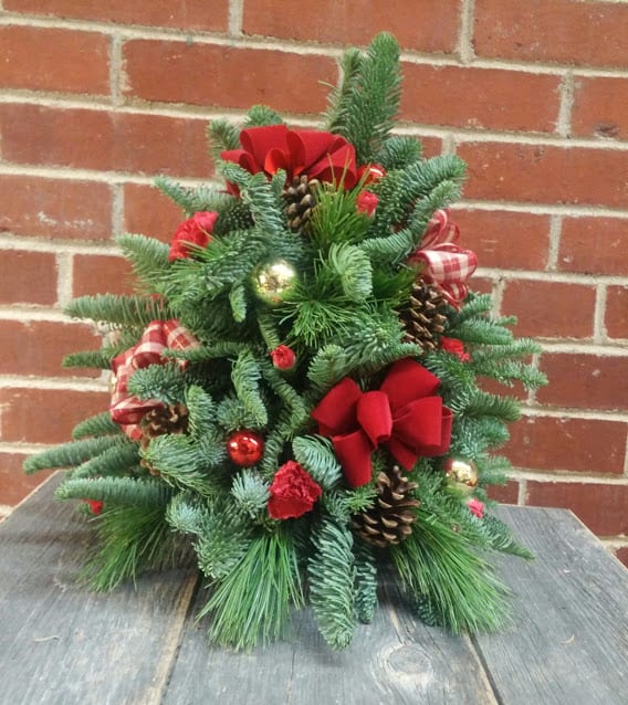 O' Christmas Tree - An adorable table top Christmas tree made from fresh evergreen.  Decorated with pine cones, bows, red mini carnations and glass balls.  We can change around the colors however you would like.  It stands 16 inches tall