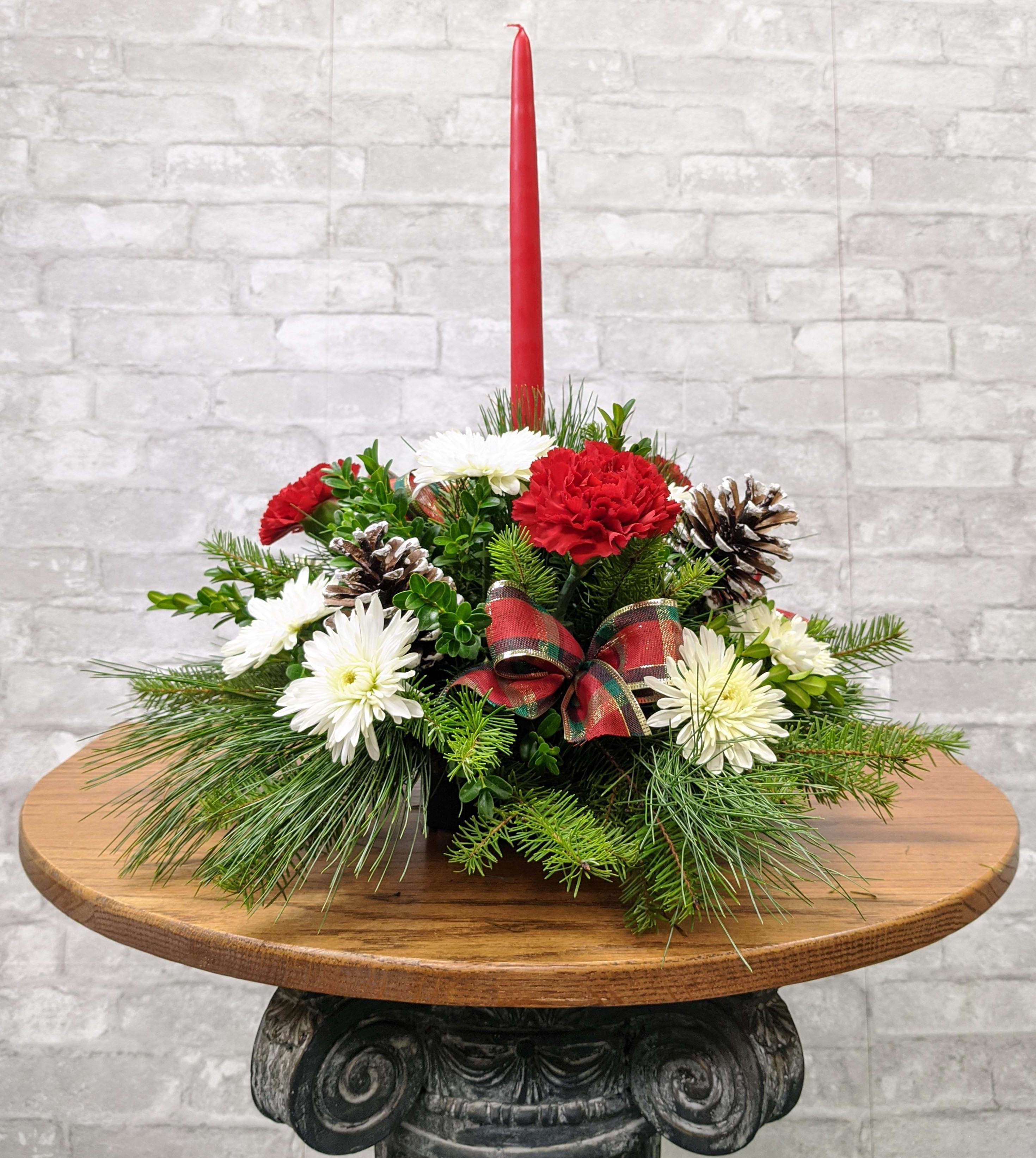 Noel Centerpiece FG - Petite round centerpiece with single taper candle.  Christmas greens, carnations and poms and pine cones.  Approximately 10&quot; wide X 17&quot; high.
