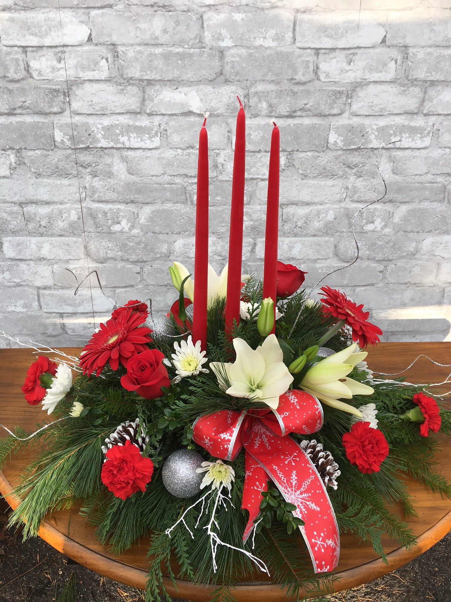 Yuletide Christmas Centerpiece FG - Lovely Oblong centerpiece with three taper candles.  Christmas greens, Christmas balls,  roses, lilies, pretty bows and frosted branches.    Approximately 21&quot; long X 19&quot; high.