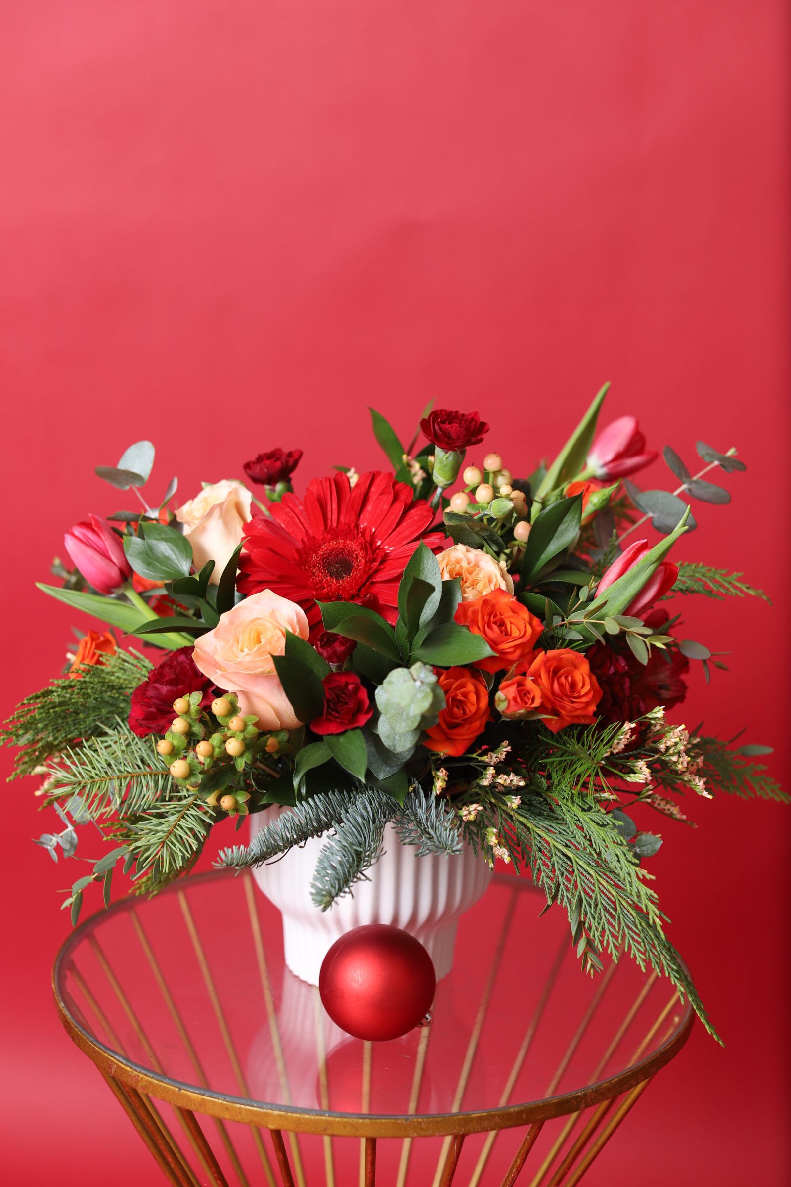 Frosted Citrus Charm - This vibrant winter arrangement combines rich reds, warm peaches, and lively oranges, set against the sleek elegance of a modern white compote. The bold, seasonal hues contrast beautifully with the crisp, cool tones of winter, creating a stunning, contemporary centerpiece that brings warmth and brightness to any space during the colder months. Frosted Citrus Charm offers a perfect balance of color and style for the holiday season or as a thoughtful gift.