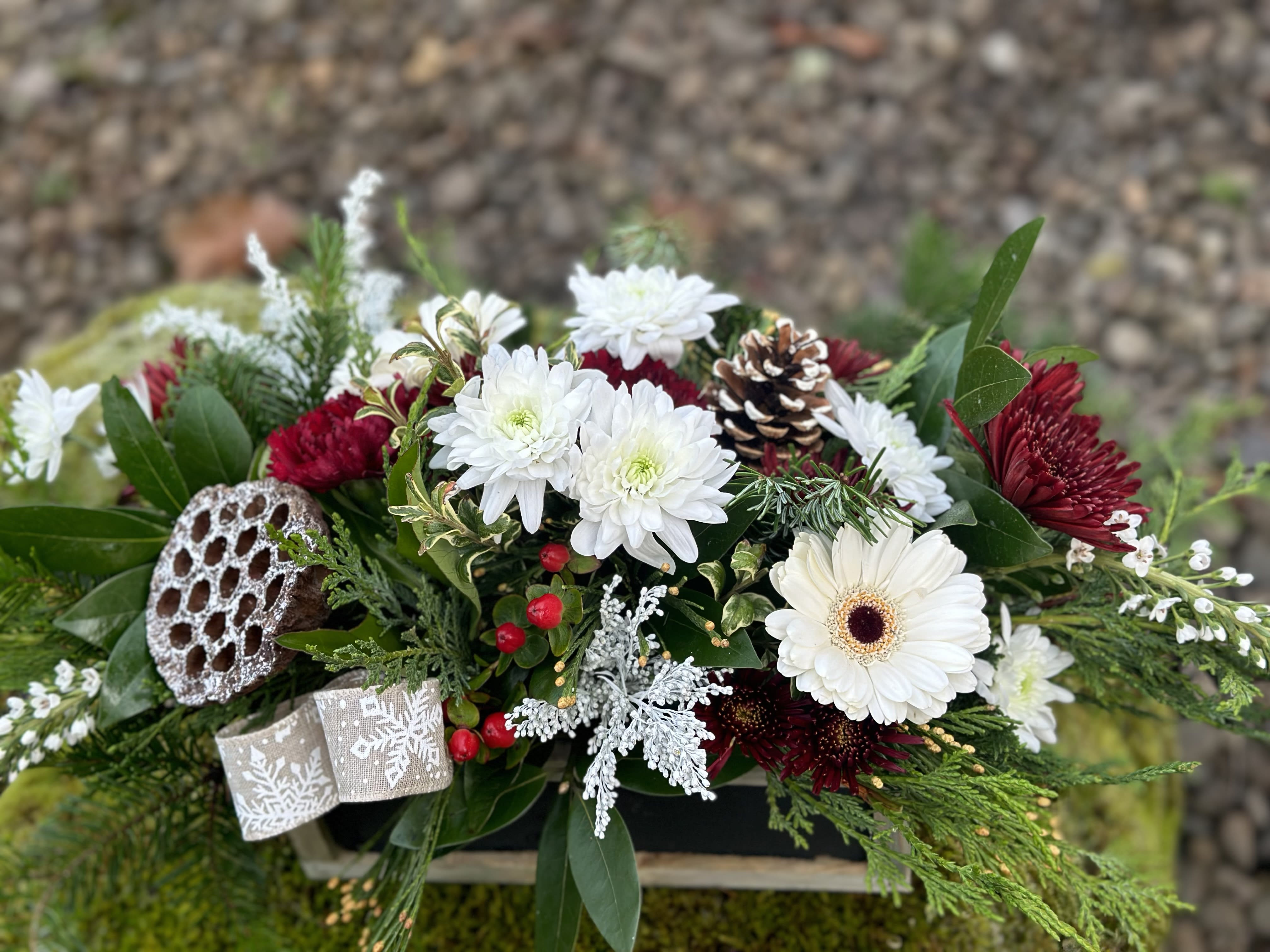 Center of the Holiday  - Low profile holiday centerpiece .  Mix of Red and white flowers may contain roses, mums , carnations or gerber daisies . Accented with berries, snowy pod and /or pinecones. Suitable for a dinner table with flowers in all sides . Standard price is in a low profile green tray. Deluxe and Premium includes a holiday tin. 