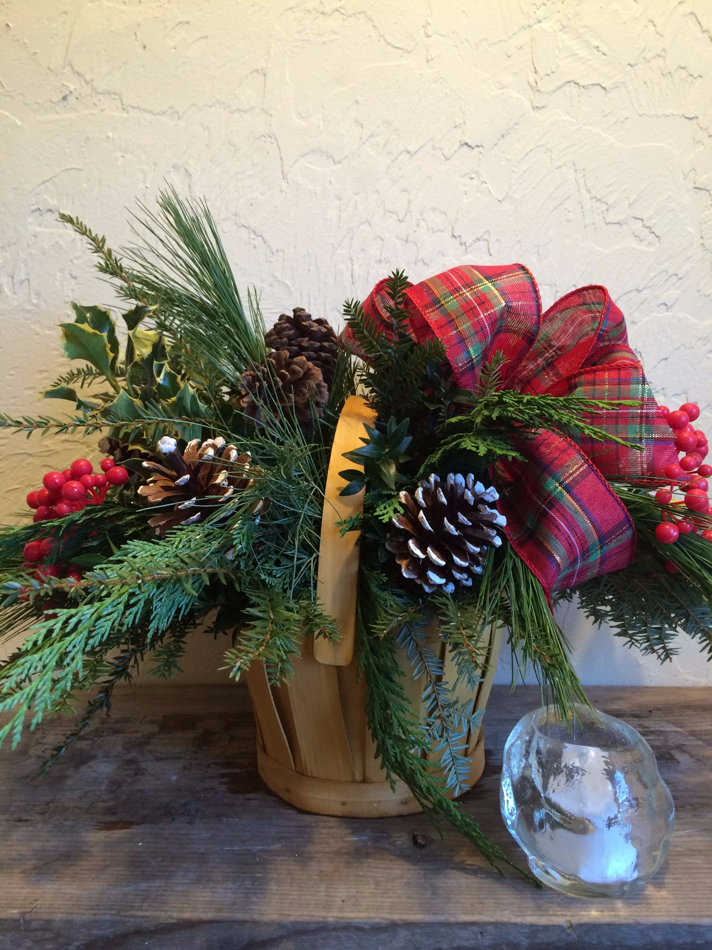 Cozy Christmas  Basket #ccb - Adding warmth and a homespun look to your Christmas décor, this fresh and fragrant floral arrangement is a wonderful way to bring color and life to any corner of the home. An assortment of Christmas greens and variegated holly are arranged to perfection in a rectangular stained woodchip basket, accented with clusters of red berries, natural pinecones, and a festive red plaid ribbon. A wonderful holiday gift for your relatives, neighbors, or friends throughout the yuletide season ahead. 
