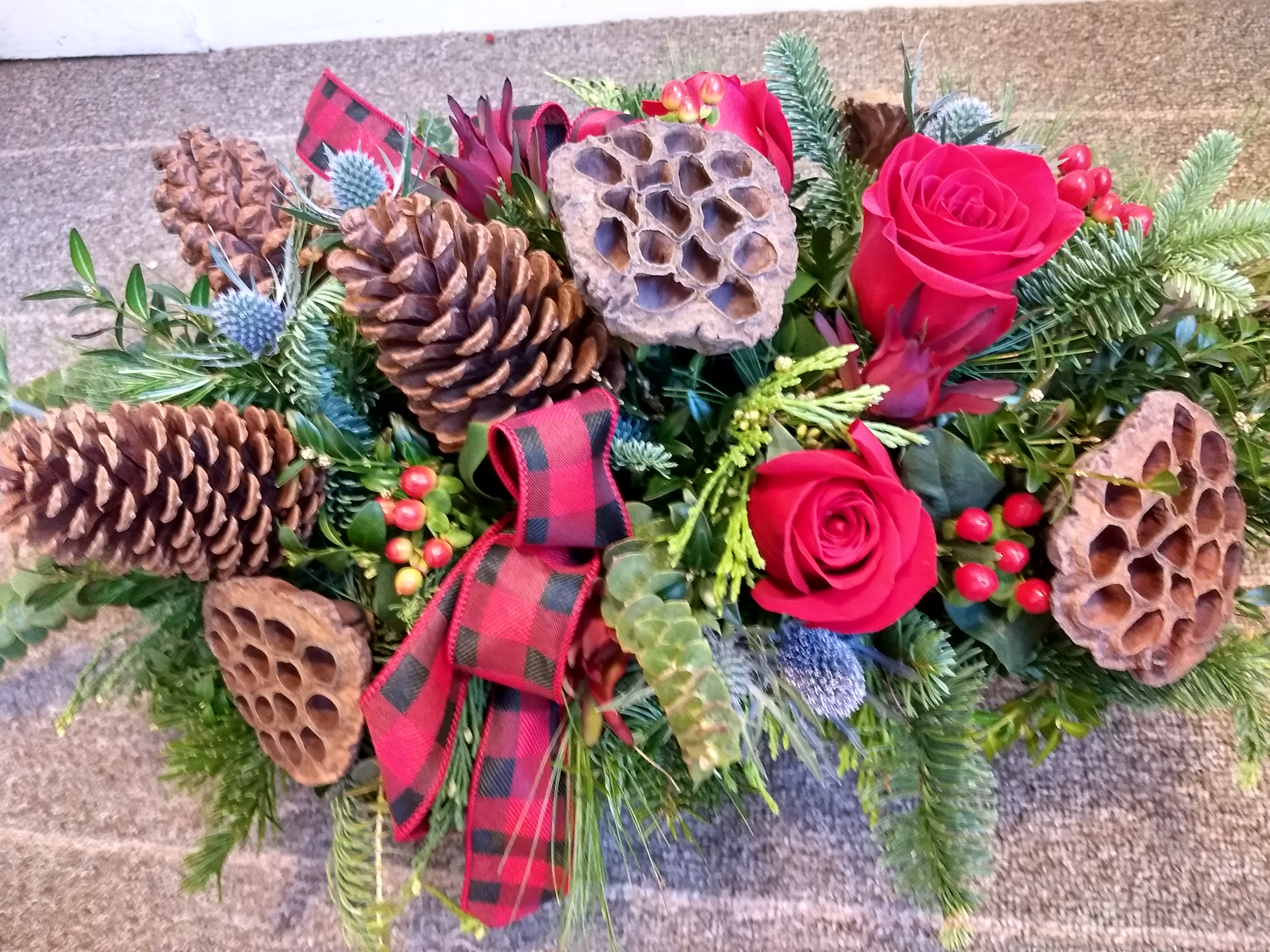 Cranberry Bog - This stunning bouquet is handcrafted to bring the cozy rustic feel of the holidays into you or home. An array of rich red roses, hypericium berries, lotus pods and mixed winter greens. The charm or a cape cod winter.