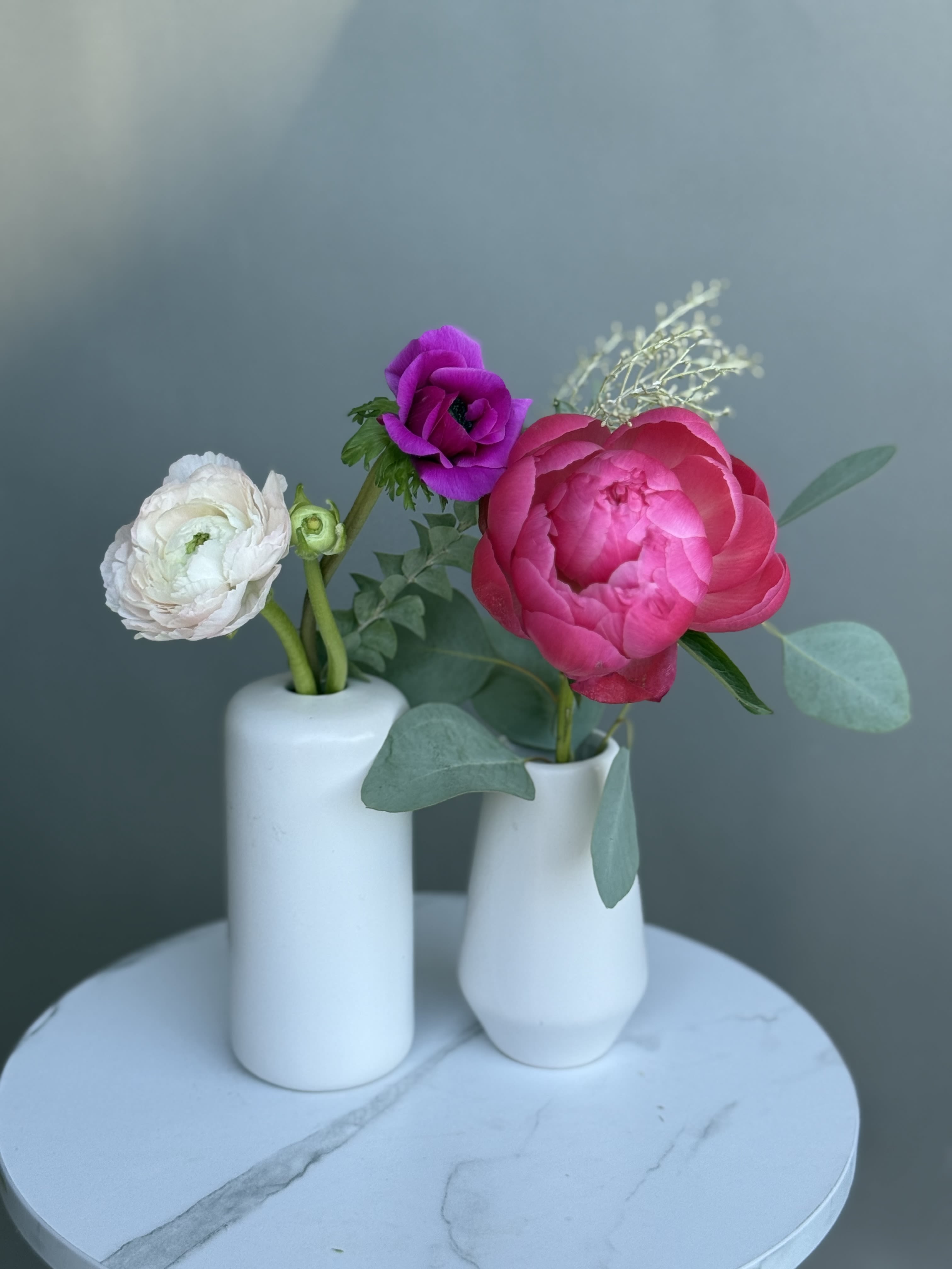 Love trio.  - COLORS WILL VARY. Peony, ranunculus and anemone with greens in moderm ceramic vases. 