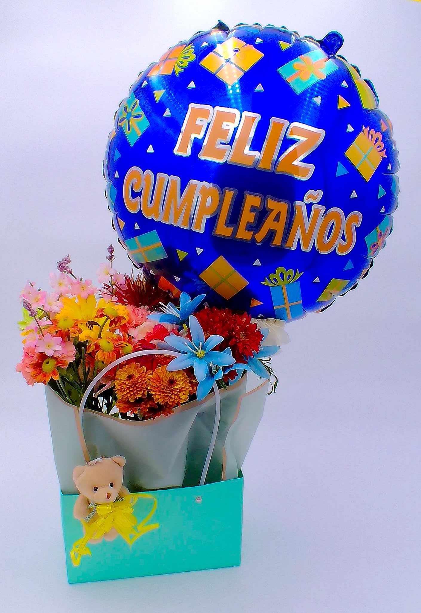 &quot;Feliz Cumpleanos&quot; Flower Gift Bag with Teddy Bear - Mixed Fresh Flowers (14–16 stems): a colorful blend of 8 carnations, 2 chrysanthemums, and 4 daisies. 18-inch Feliz Cumpleaños Foil Balloon (1 pc) Mini Teddy Bear (11 cm/6 cm) (1pc) Reusable Gift Bag (32.5cm*22cm*13cm) Total Weight:700 g Ideal for: Birthdays, Surprise parties, and home deliveries, Cheerful “thinking of you” gifts for loved ones, and Spanish celebrations.